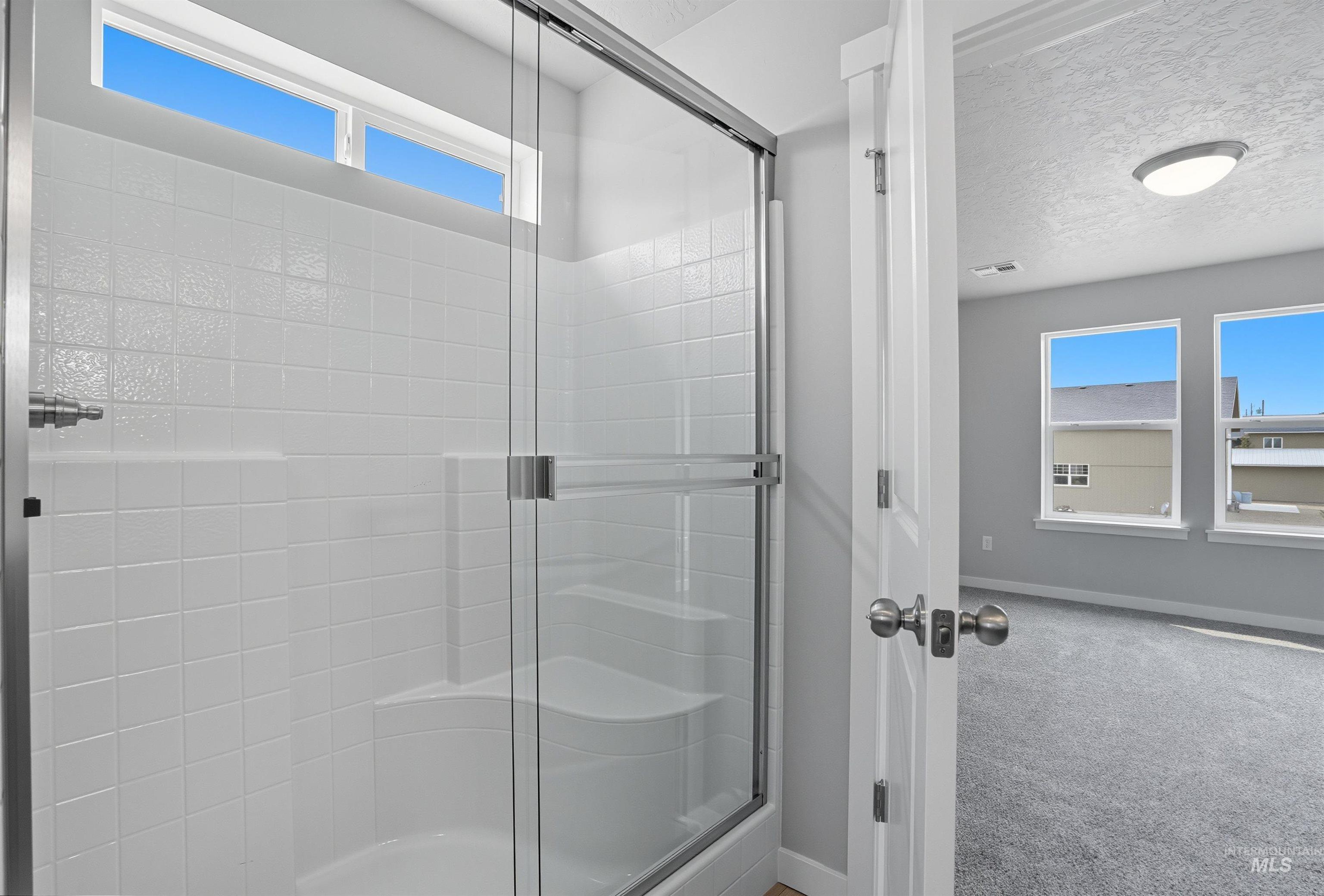 Shower enclosure with clear glass sliding doors, white square tile surround, integrated shelving, and a transom window