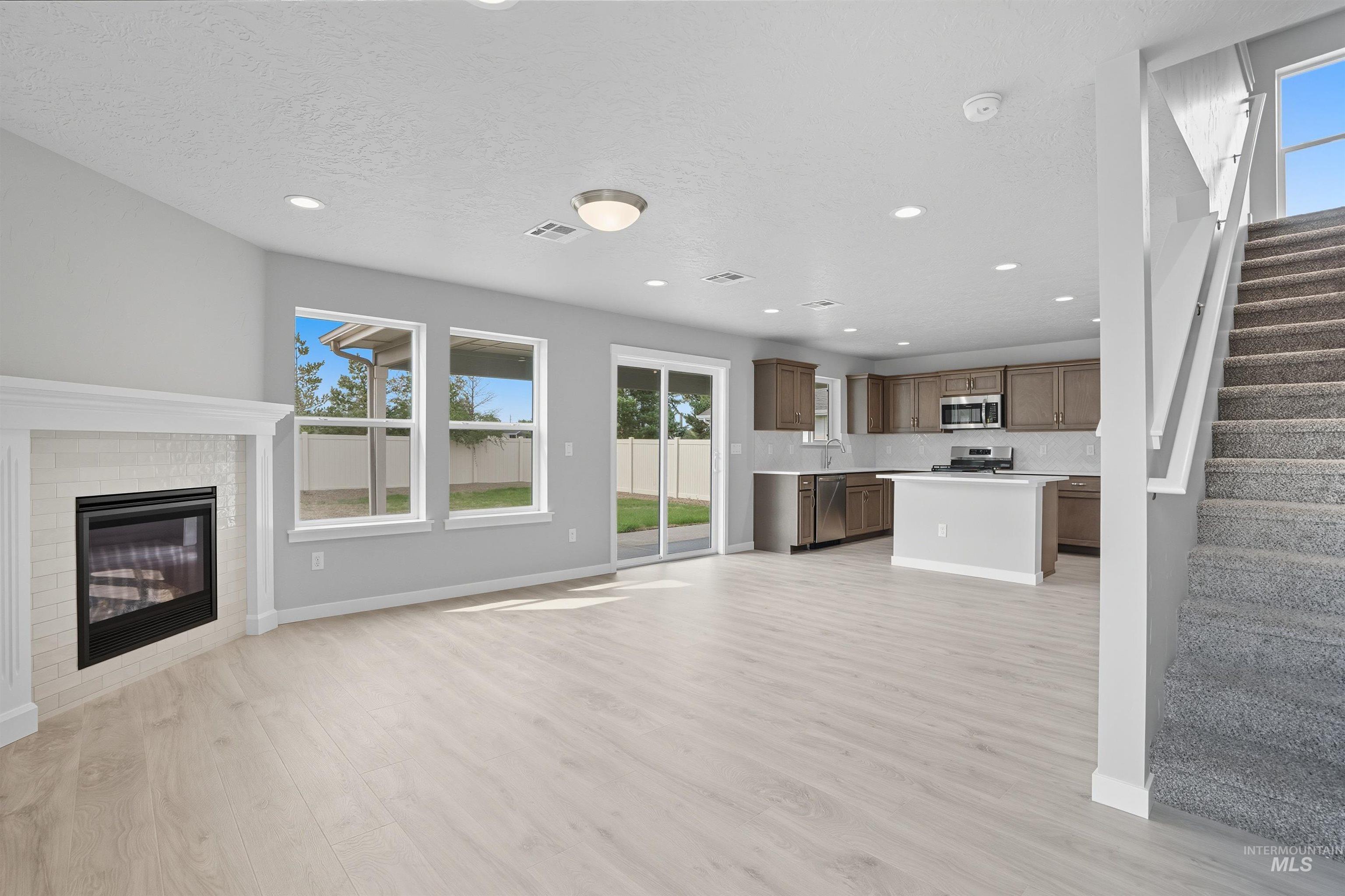 Open-concept living space featuring light wood-finish flooring, a contemporary fireplace with a white mantel and tile surround, and recessed lighting
