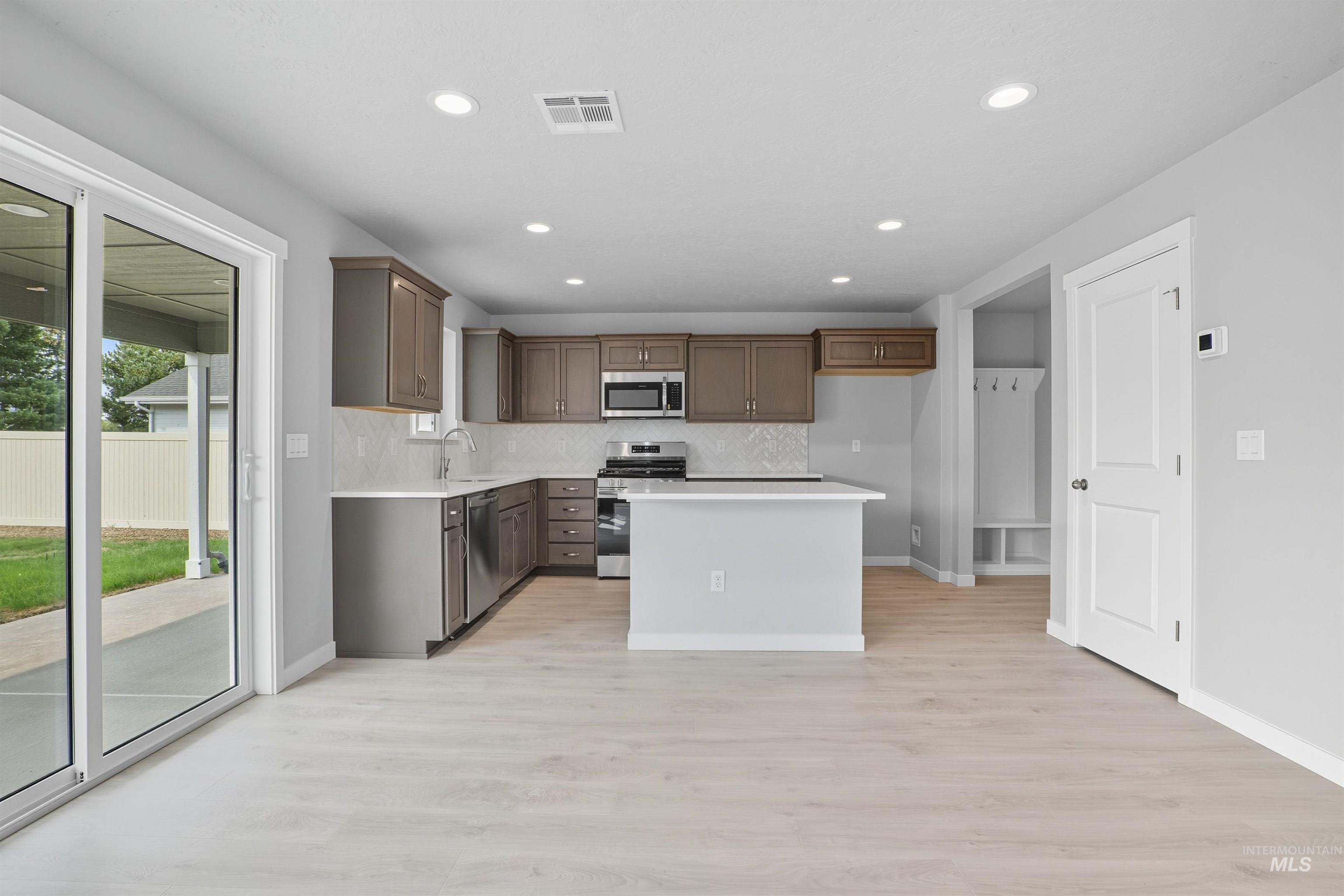 Open-concept living area featuring light wood-finish flooring, recessed lighting, and a modern kitchen