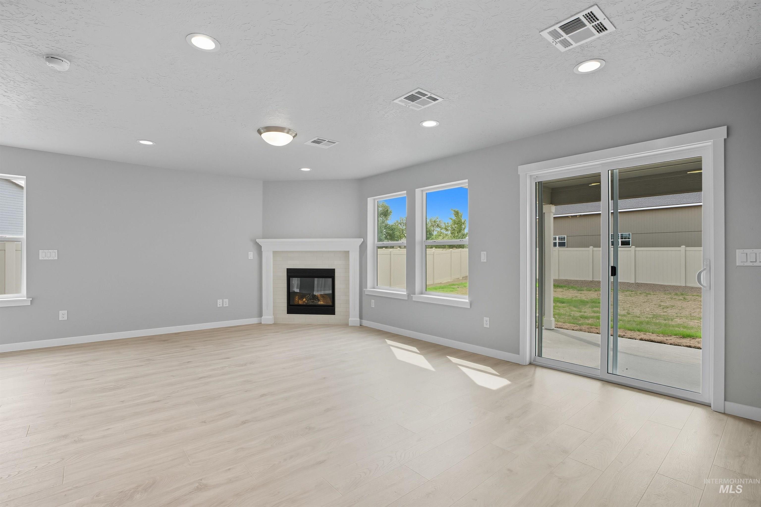 Spacious room featuring wood-finish flooring, a contemporary fireplace with a white mantel, recessed lighting, and multiple windows