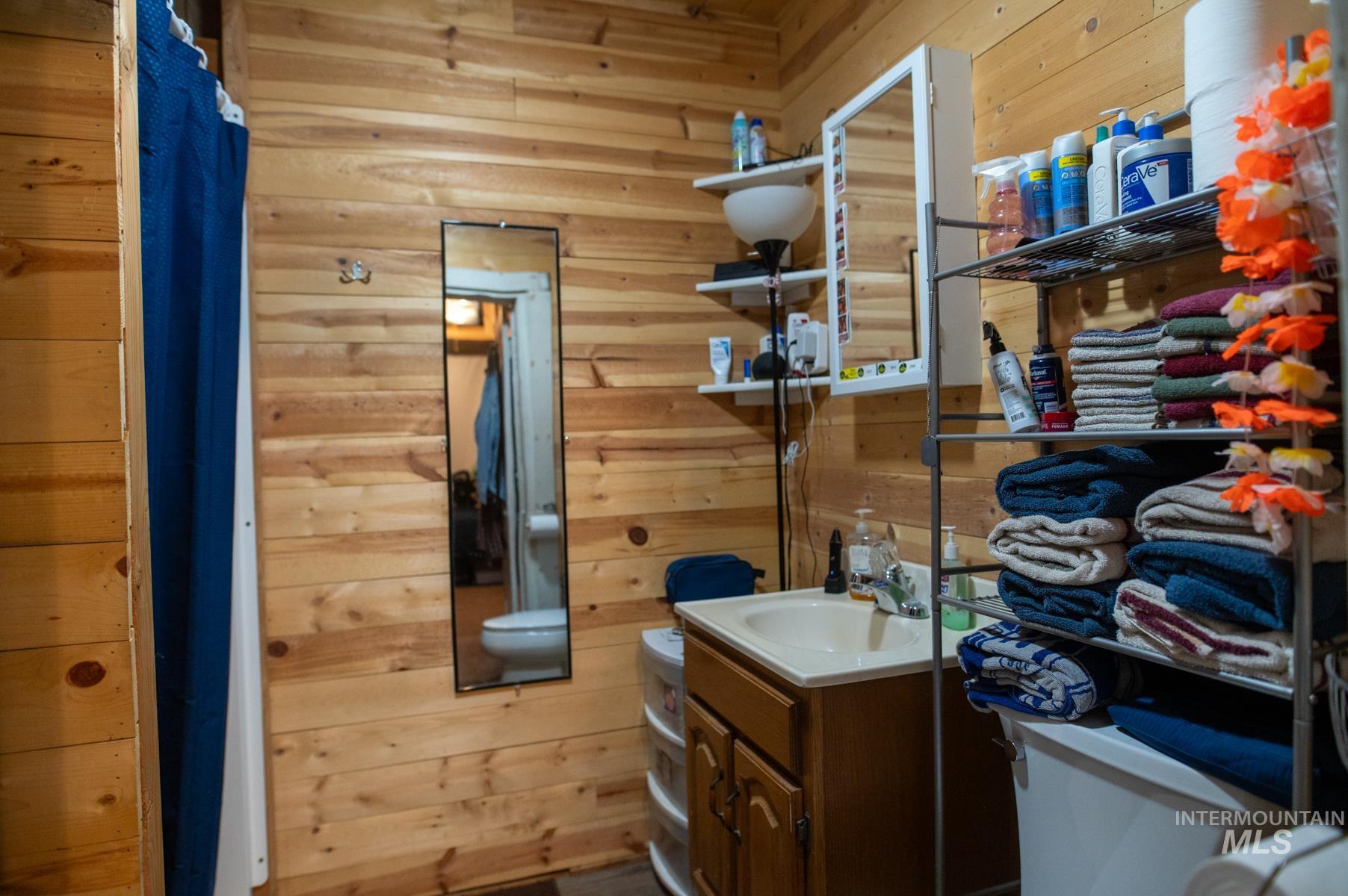 Bathroom featuring wood-paneled walls, a single vanity with a cream-colored sink and wood cabinetry, and a wall-mounted mirror