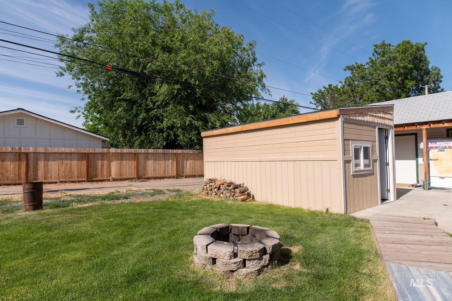 Expansive backyard featuring a stone fire pit, wood privacy fencing, and a separate storage shed with an awning