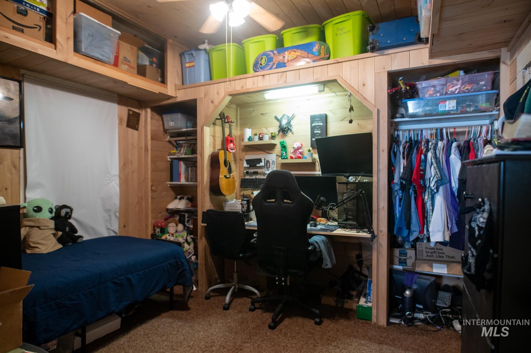 Wood-paneled room featuring a built-in desk area with overhead lighting, a ceiling fan, and integrated open shelving