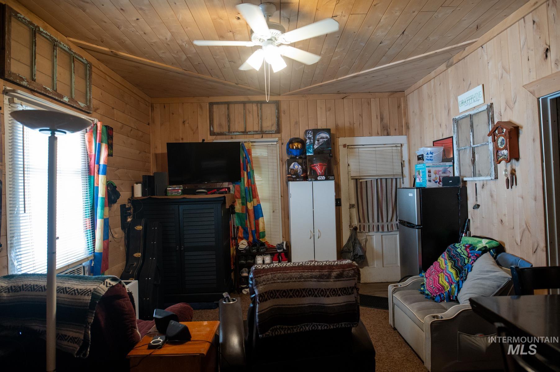 Interior space featuring wood-paneled walls, a wood-finish ceiling with a ceiling fan, and a window with horizontal blinds