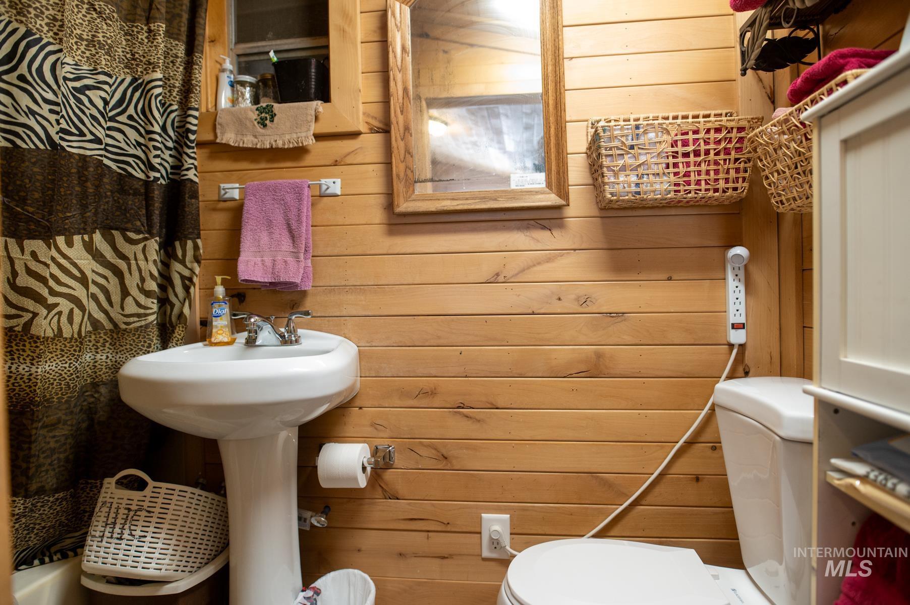 Bathroom featuring horizontal wood paneling, a white pedestal sink with chrome fixtures, a white toilet, and a framed mirror