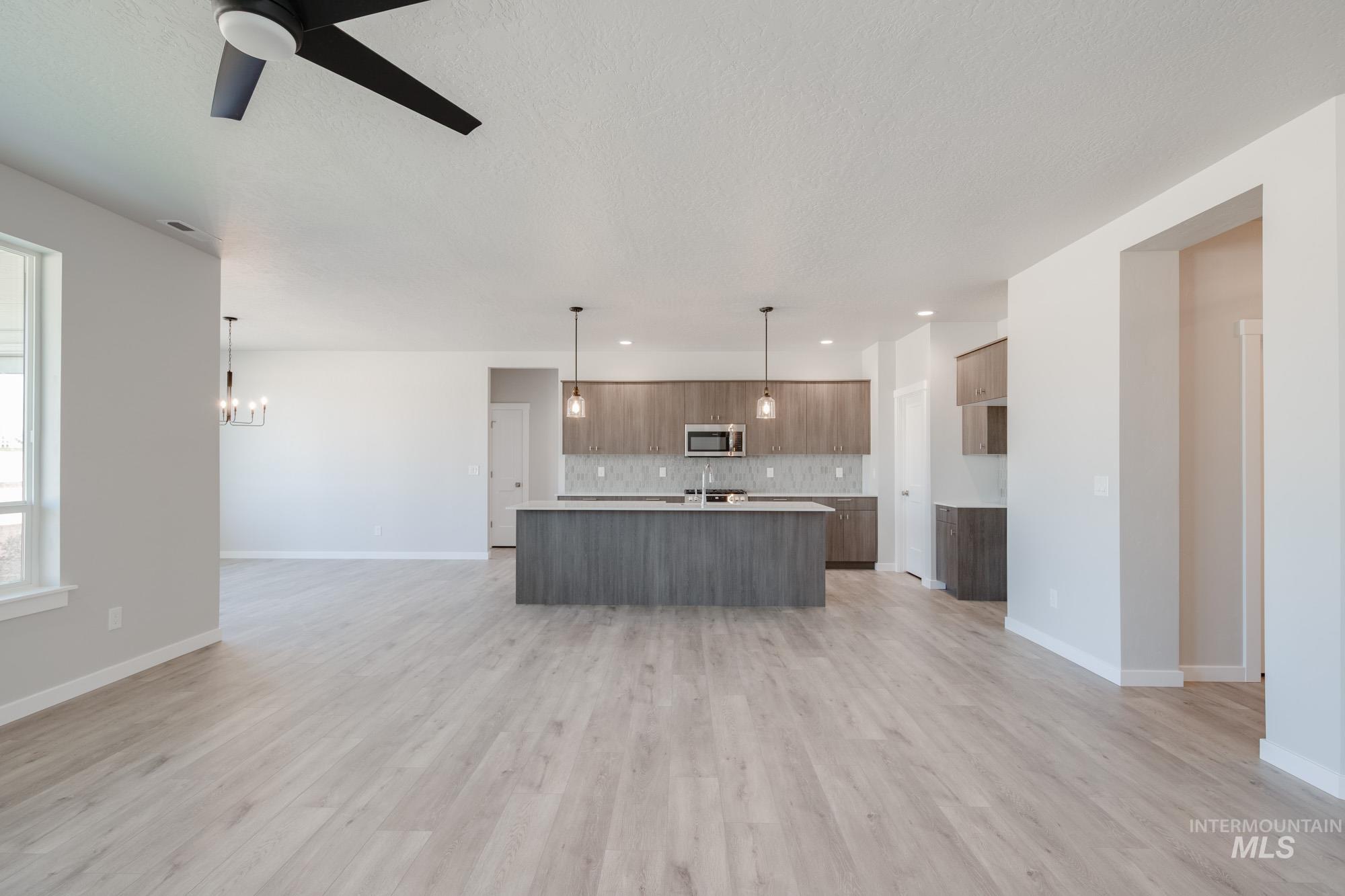 Kitchen with open floor plan, light countertops, a kitchen island with sink, decorative light fixtures, and modern cabinets