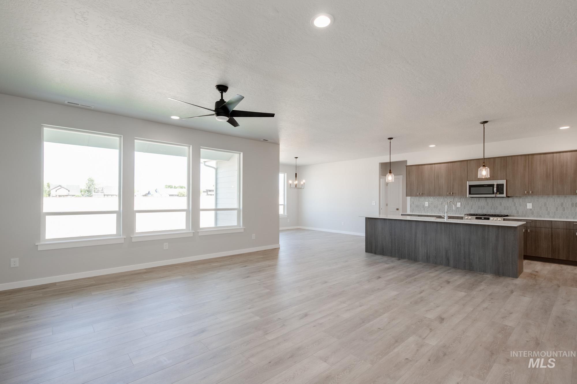 Kitchen featuring an island with sink, open floor plan, decorative light fixtures, modern cabinets, and light wood finished floors