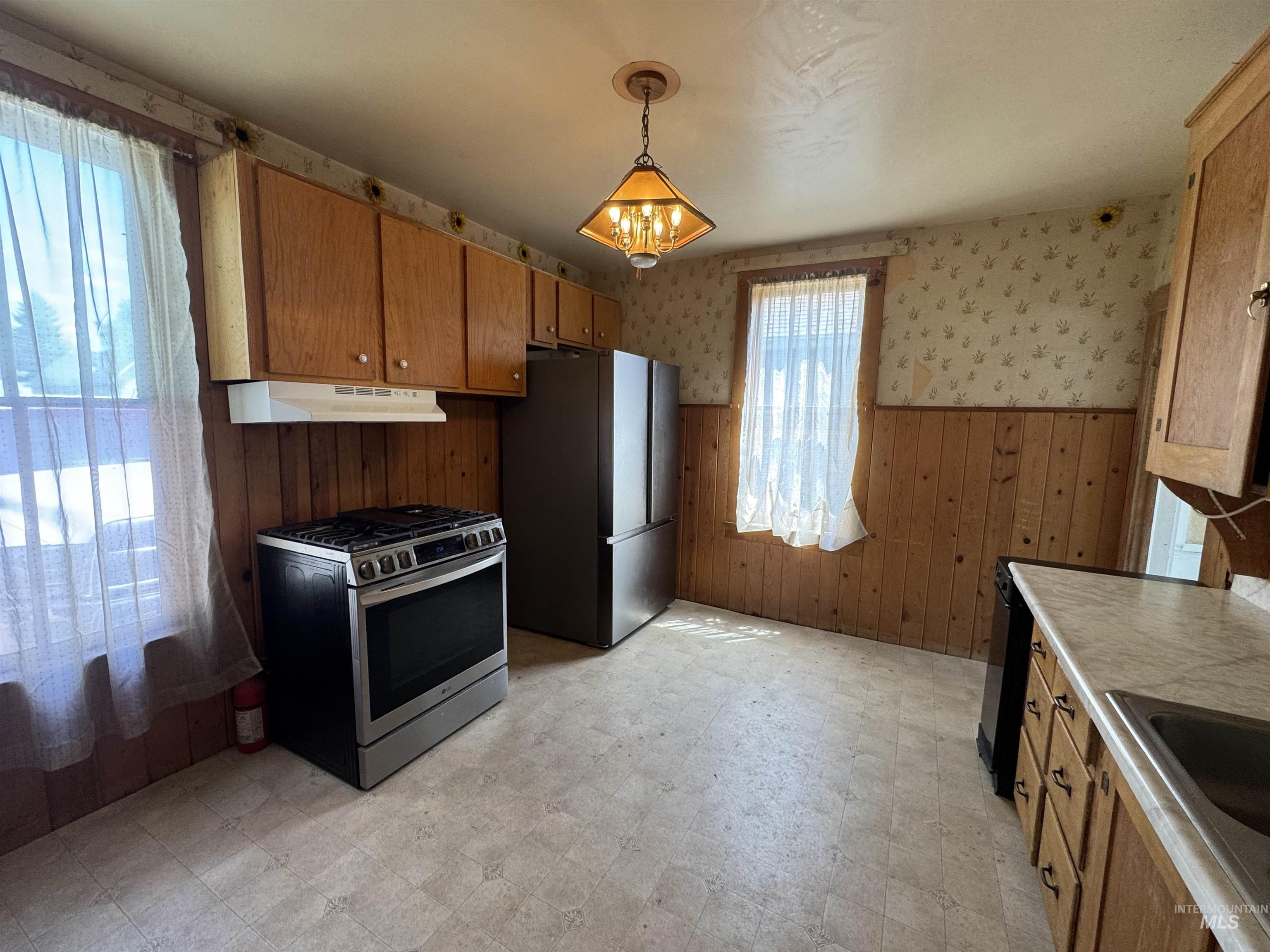 Kitchen with light floors, wainscoting, stainless steel gas range, a chandelier, and freestanding refrigerator