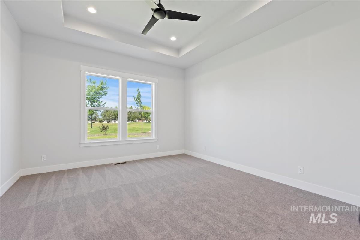 Empty room with a tray ceiling, light colored carpet, recessed lighting, and ceiling fan
