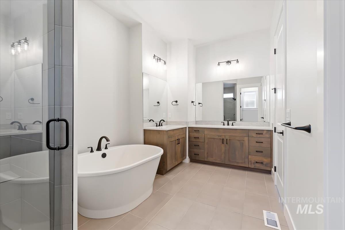 Full bathroom with a freestanding tub, two vanities, a stall shower, and light tile patterned flooring