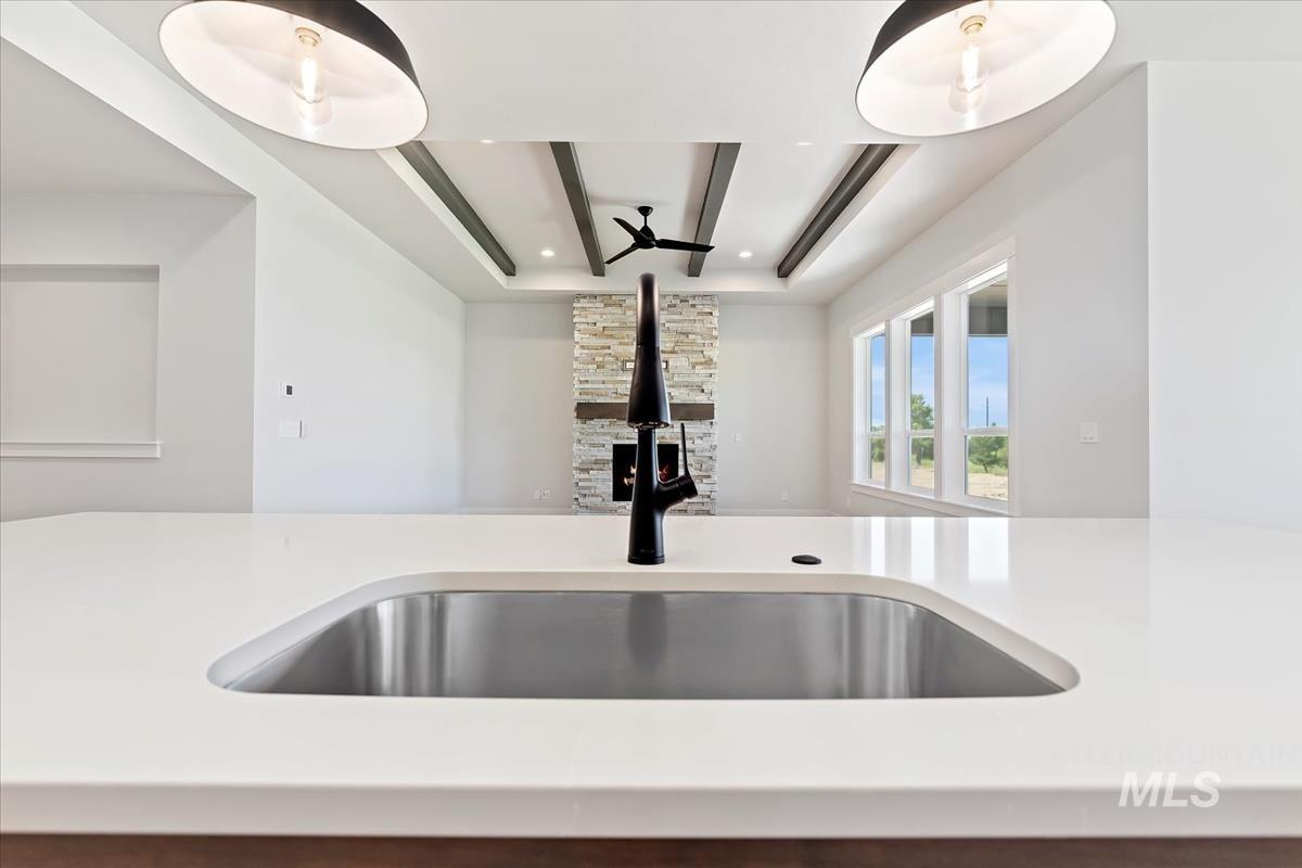 Kitchen view of beam ceiling, a ceiling fan, and light stone counters
