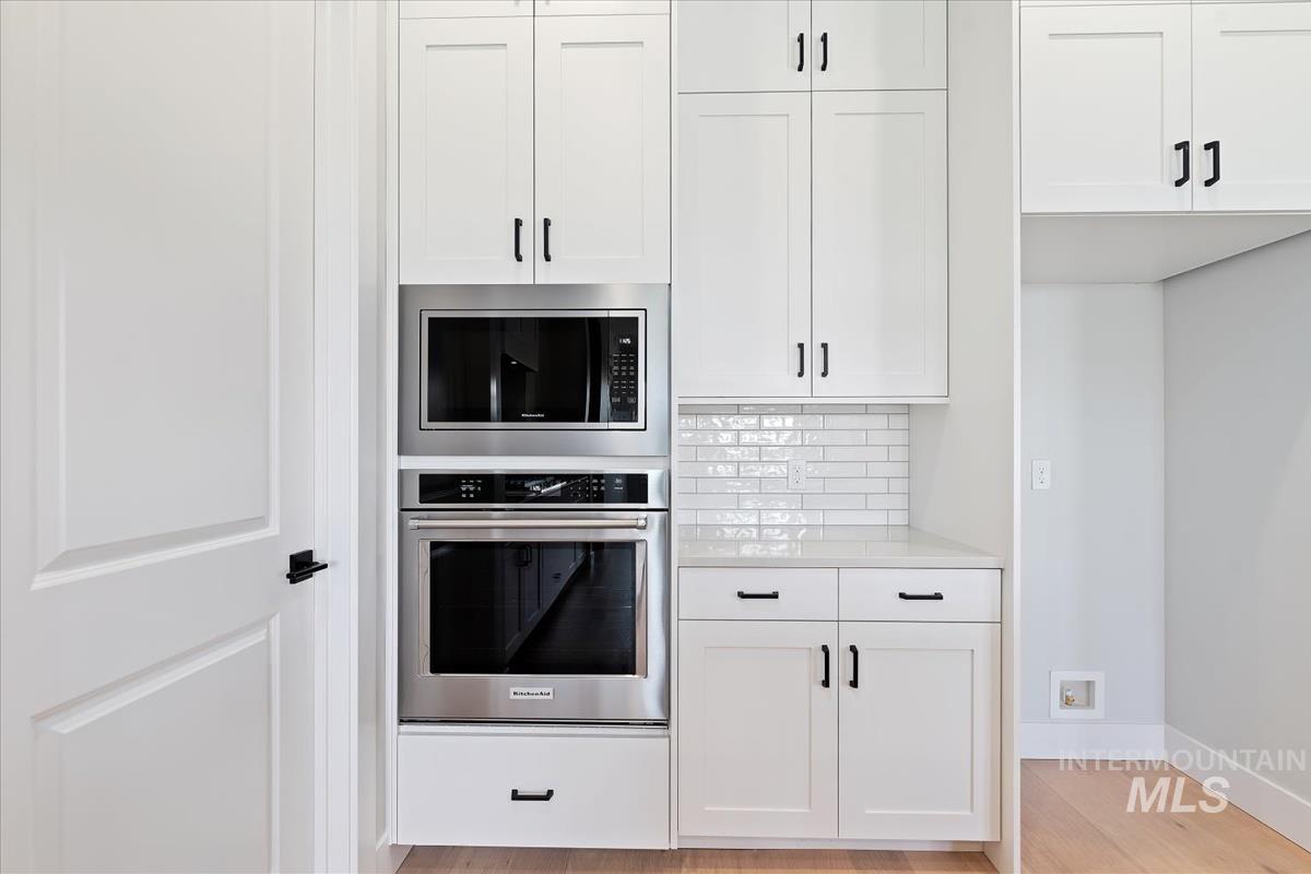 Kitchen featuring stainless steel appliances, white cabinets, light wood finished floors, and light stone countertops
