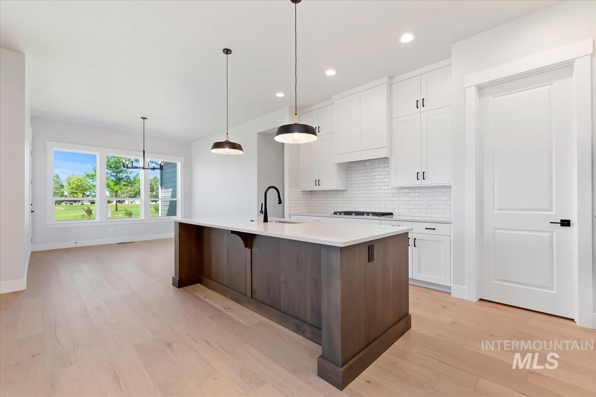 Kitchen featuring white cabinetry, tasteful backsplash, a chandelier, dark brown cabinets, and pendant lighting