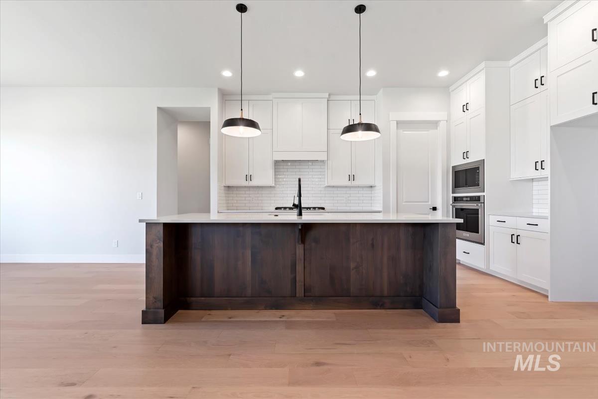 Kitchen with white cabinets, tasteful backsplash, a kitchen island with sink, pendant lighting, and dark brown cabinets