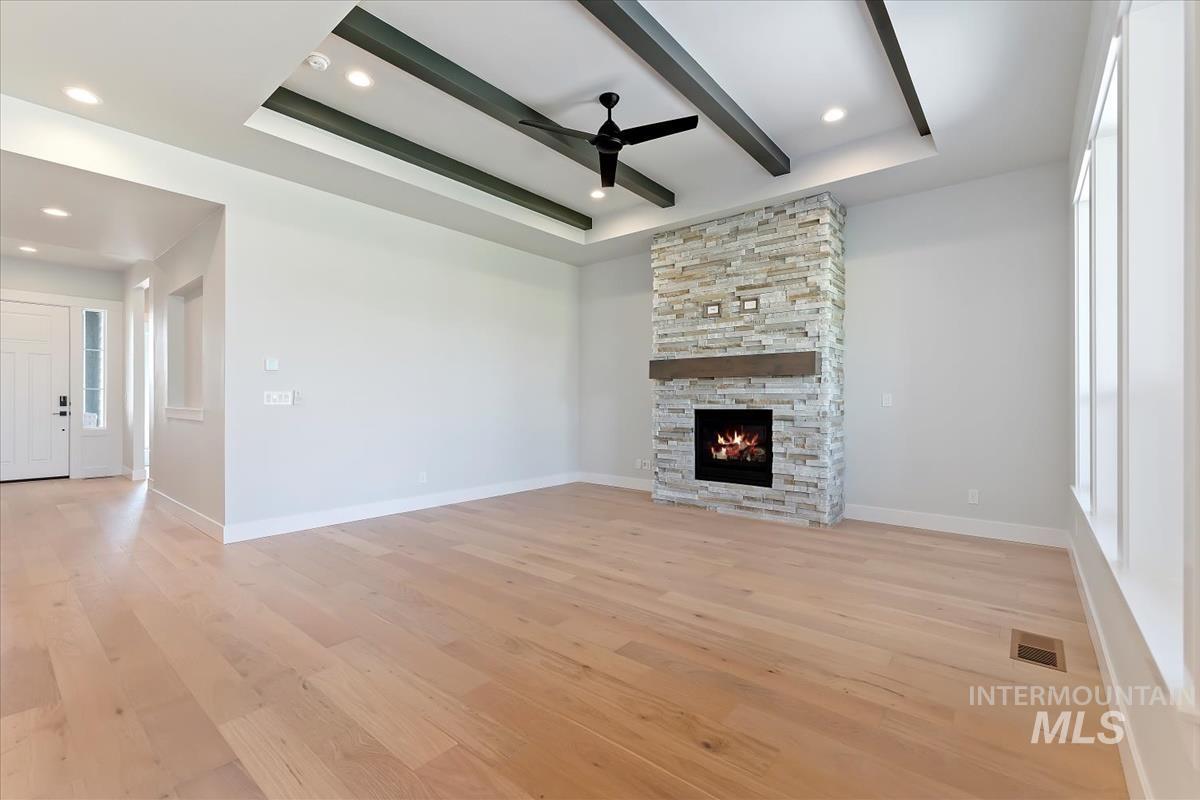 Unfurnished living room featuring light wood-type flooring, a raised ceiling, a ceiling fan, healthy amount of natural light, and beamed ceiling