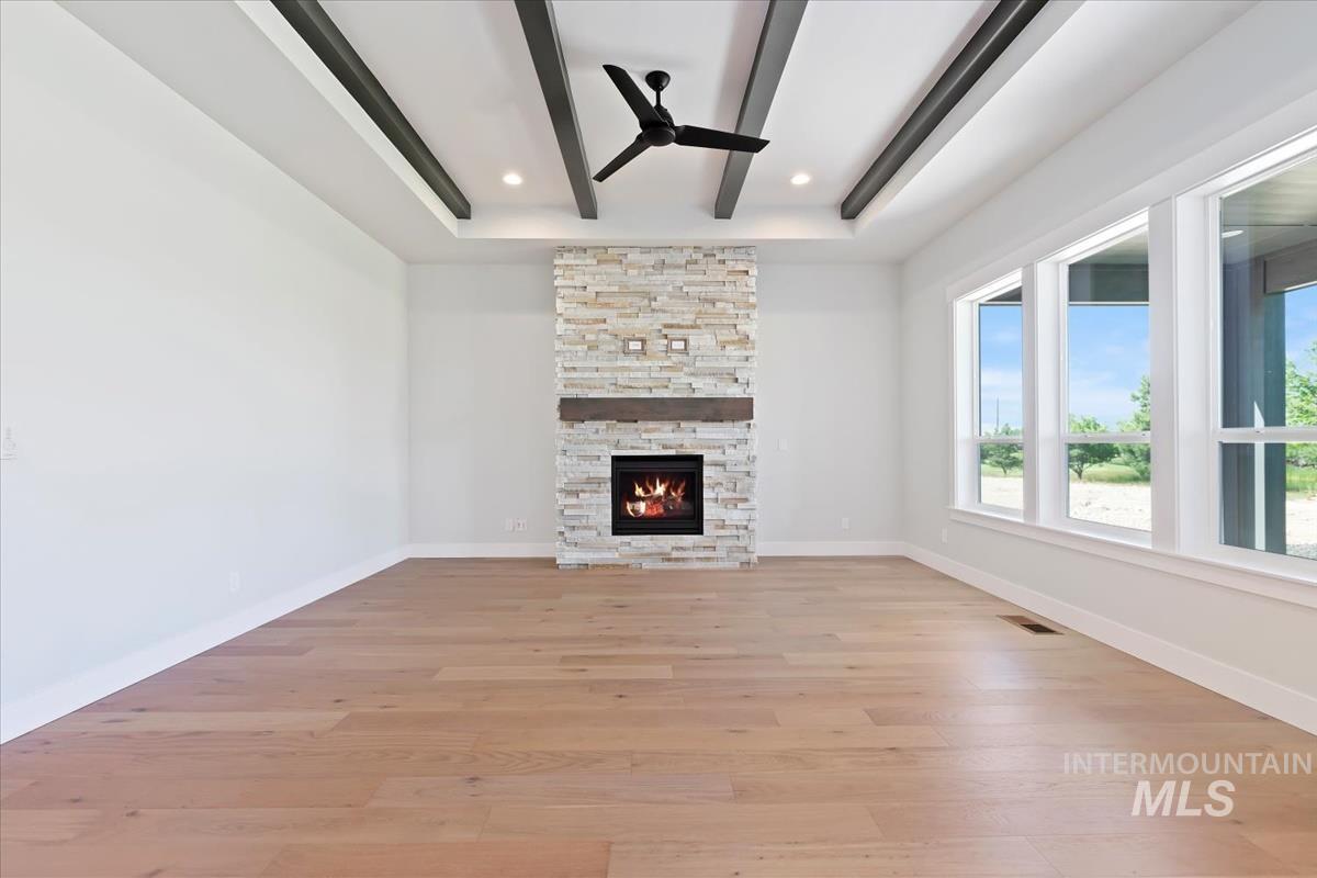 Unfurnished living room featuring ceiling fan, light wood-type flooring, a stone fireplace, beamed ceiling, and recessed lighting
