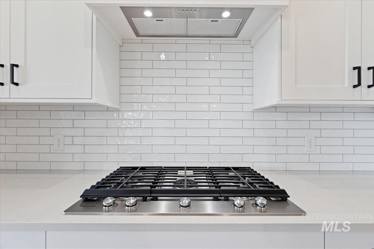 Kitchen view of extractor fan, stainless steel gas cooktop, backsplash, and light stone countertops