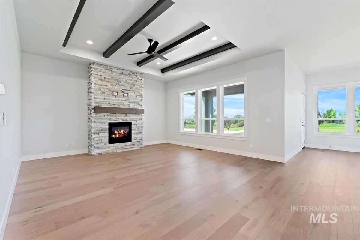 Unfurnished living room with a ceiling fan, plenty of natural light, light wood-style floors, a tray ceiling, and recessed lighting