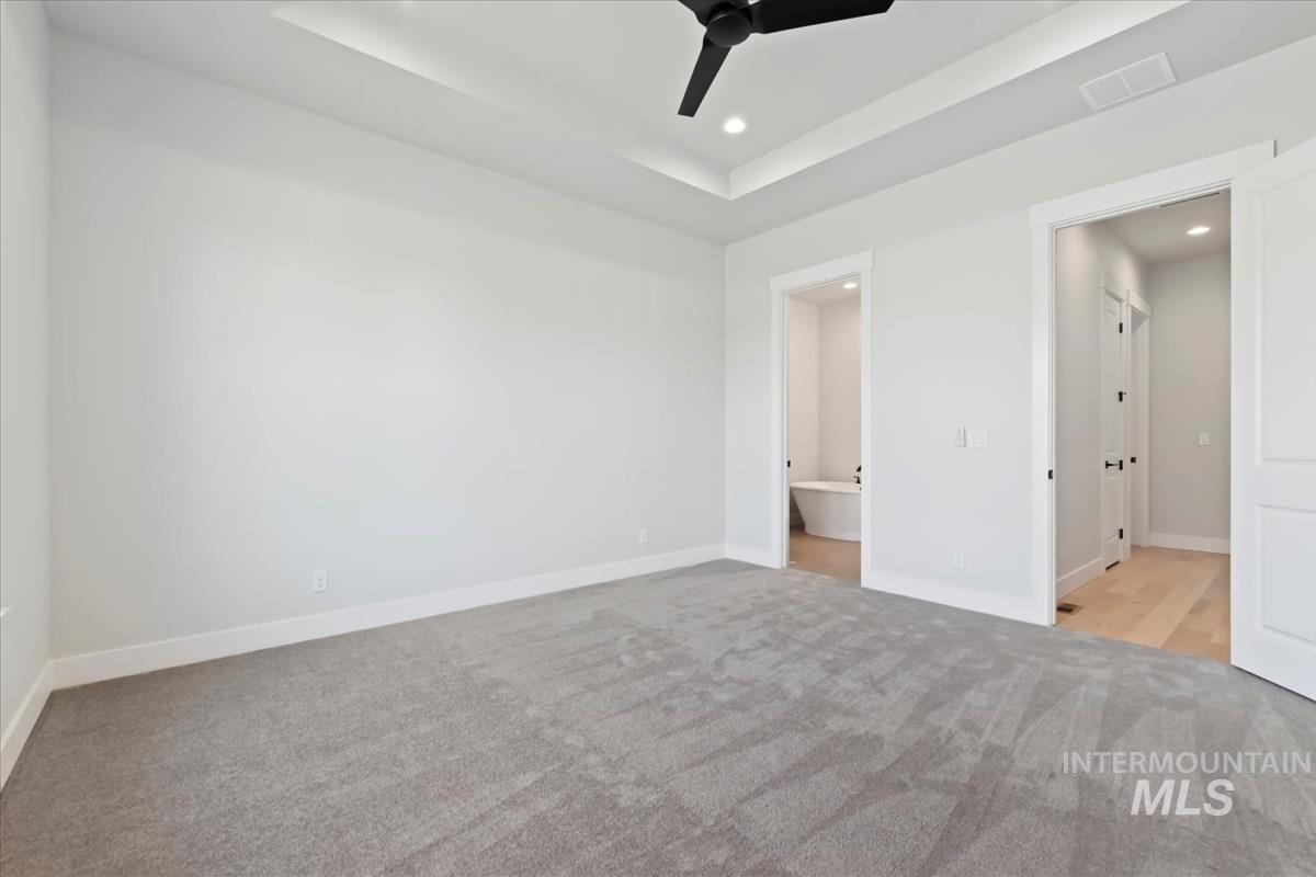 Unfurnished bedroom featuring light colored carpet, a raised ceiling, ceiling fan, recessed lighting, and ensuite bath