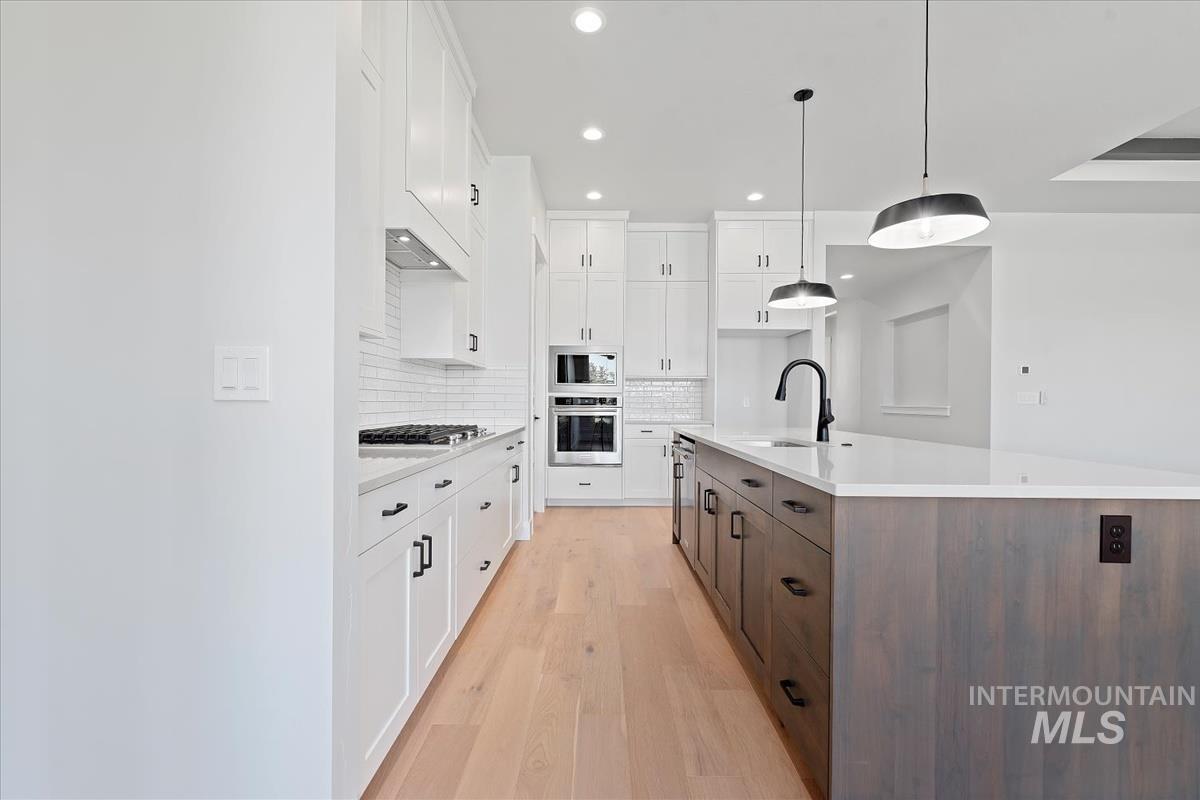 Kitchen with white cabinets, tasteful backsplash, light wood-type flooring, a kitchen island with sink, and decorative light fixtures