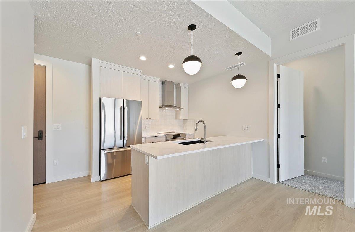 Kitchen with stainless steel appliances, modern cabinets, decorative light fixtures, a peninsula, and a textured ceiling