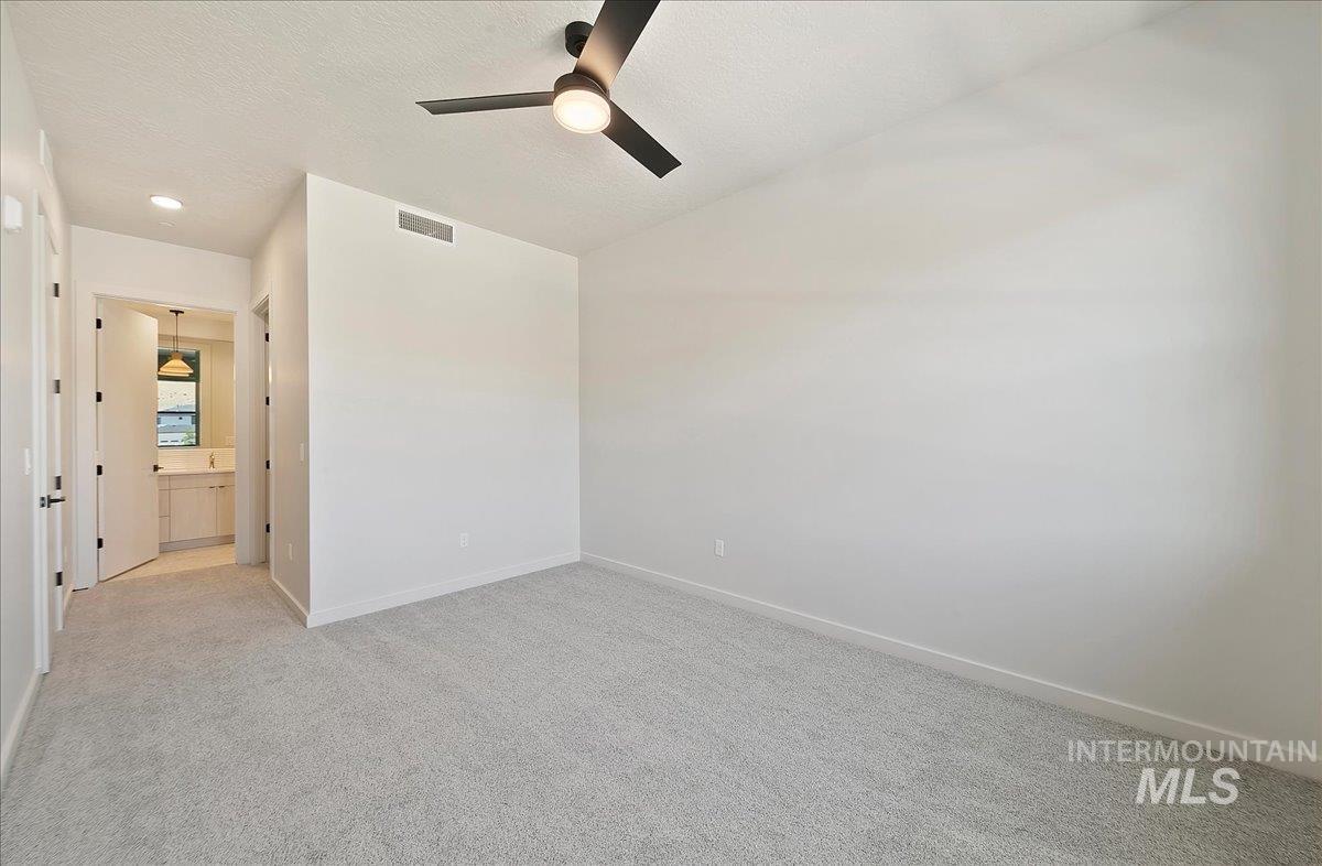 Unfurnished bedroom with light carpet, a textured ceiling, ensuite bath, and a ceiling fan