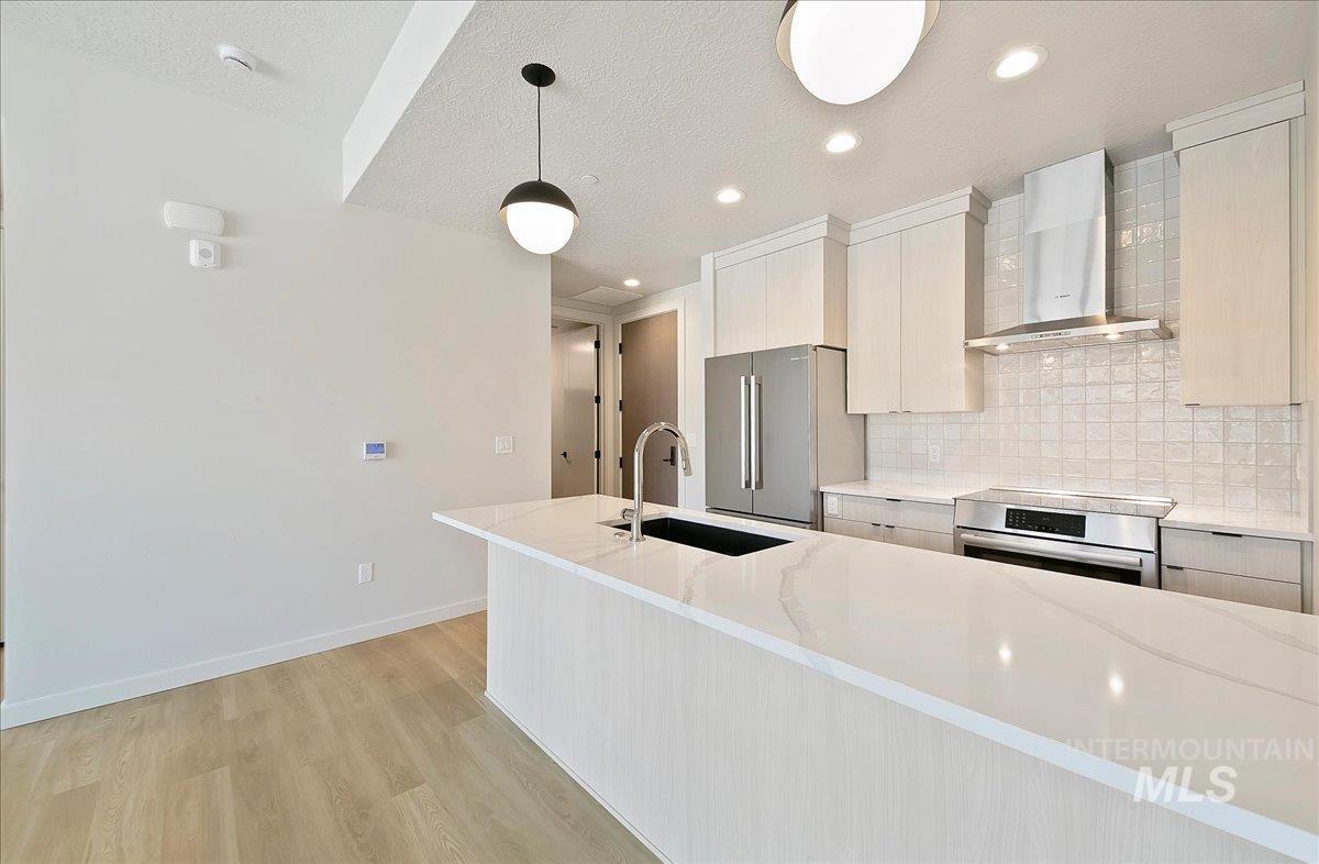Kitchen featuring wall chimney range hood, light stone countertops, modern cabinets, light wood-type flooring, and decorative backsplash
