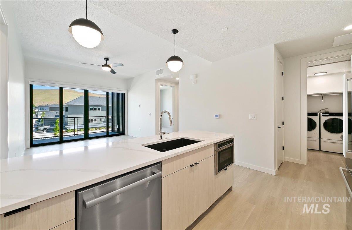Kitchen featuring light brown cabinets, a textured ceiling, stainless steel appliances, light wood-style flooring, and pendant lighting