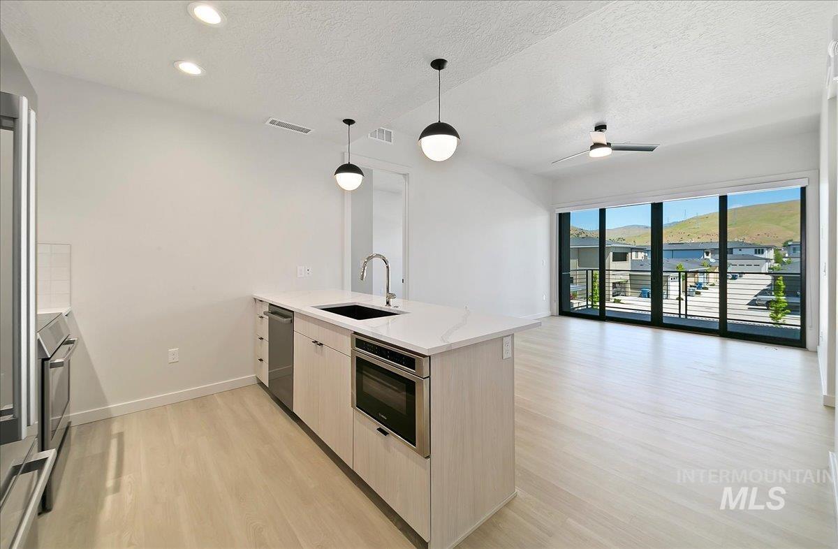 Kitchen with a peninsula, light wood finished floors, a textured ceiling, decorative light fixtures, and light stone countertops