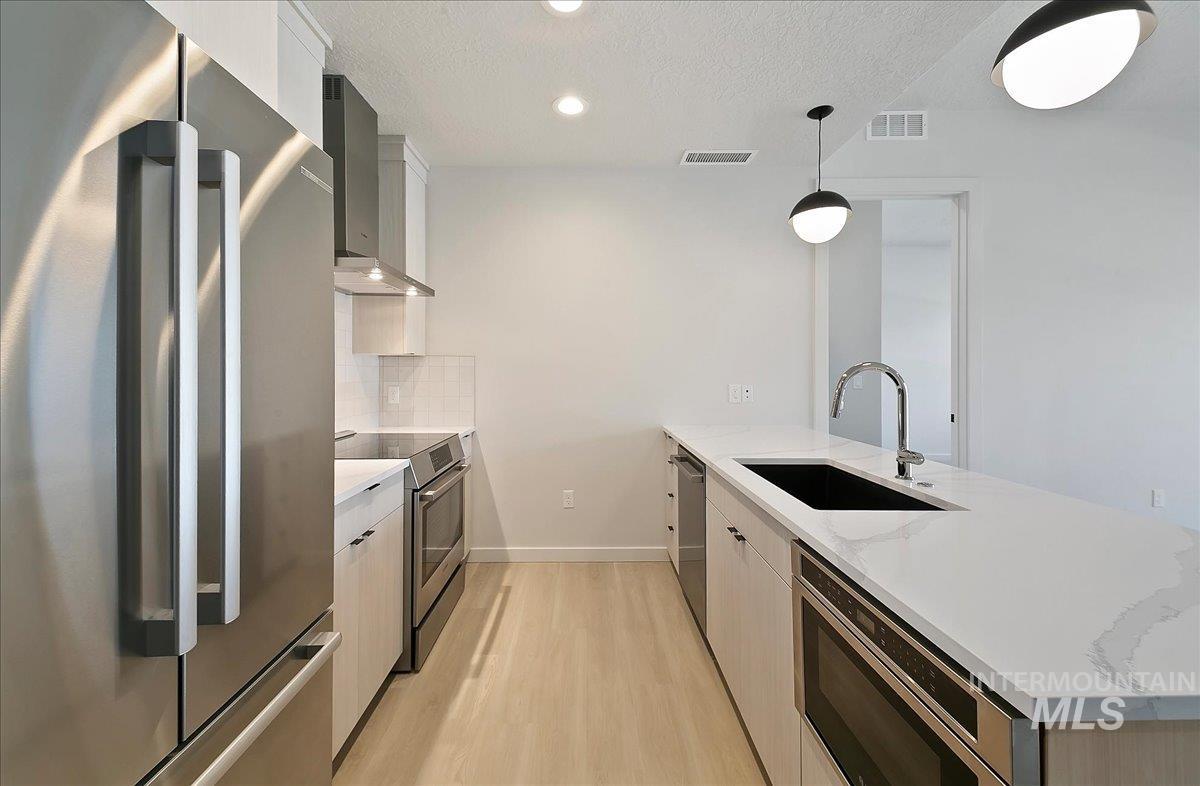 Kitchen with stainless steel appliances, a peninsula, light stone countertops, light wood-style flooring, and a textured ceiling