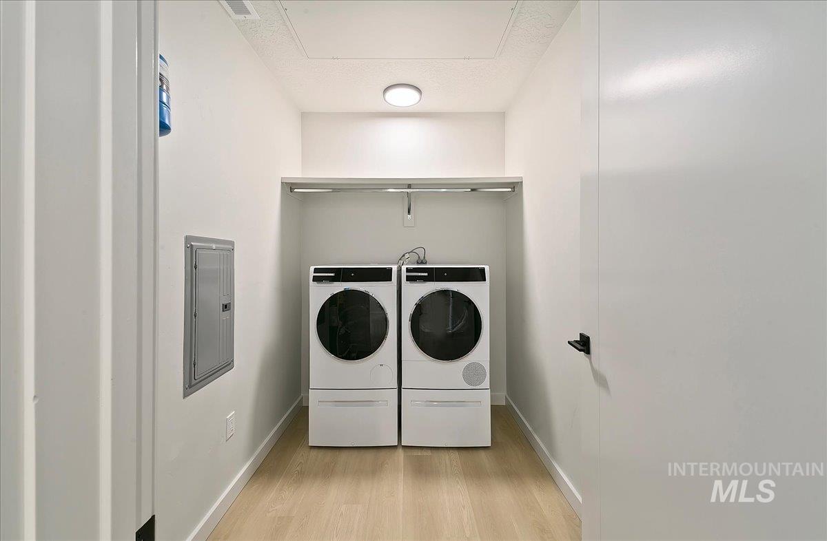 Laundry room with electric panel, a textured ceiling, and independent washer and dryer