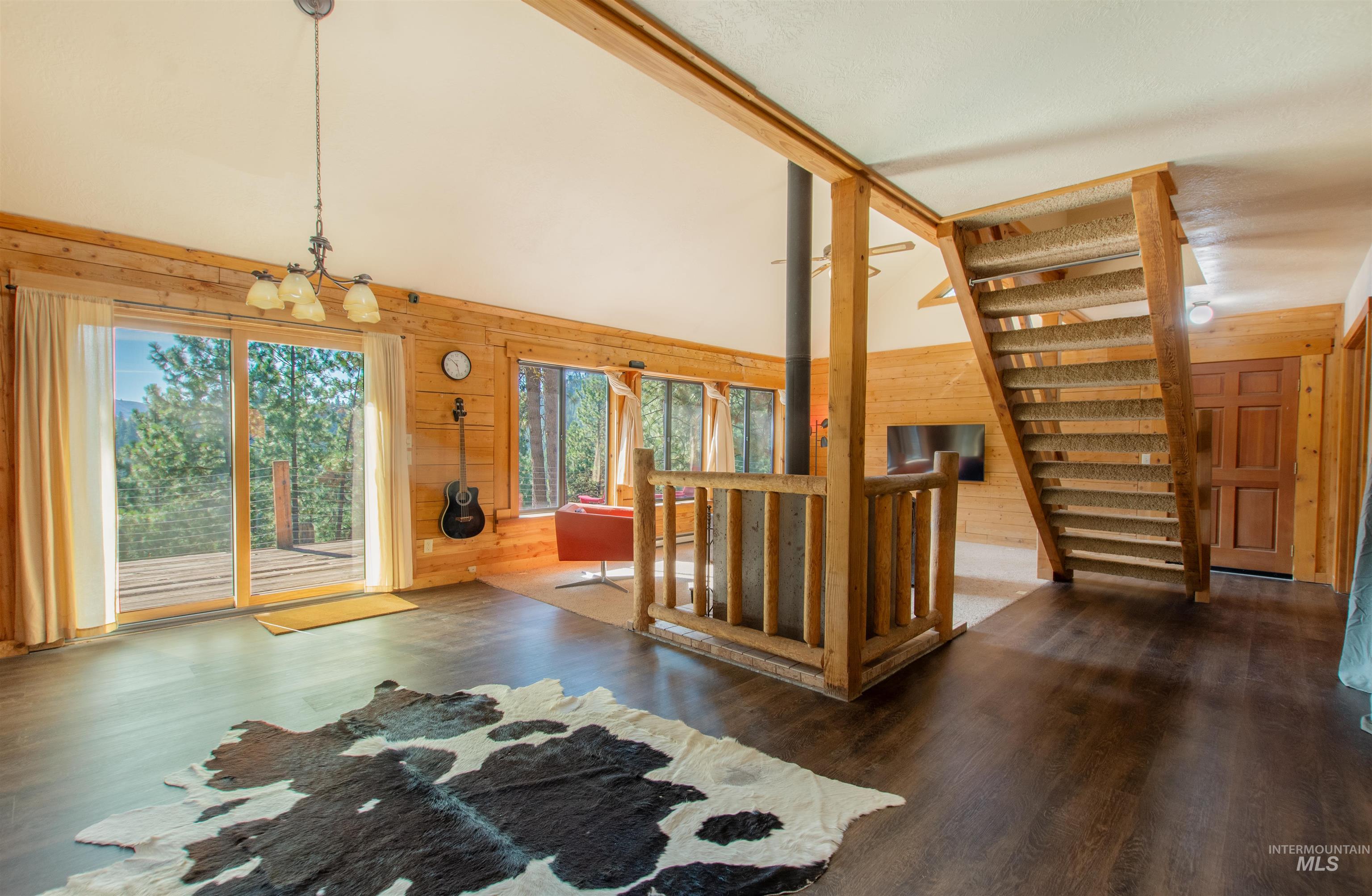 Interior space featuring wooden walls, high vaulted ceiling, wood finished floors, plenty of natural light, and a chandelier