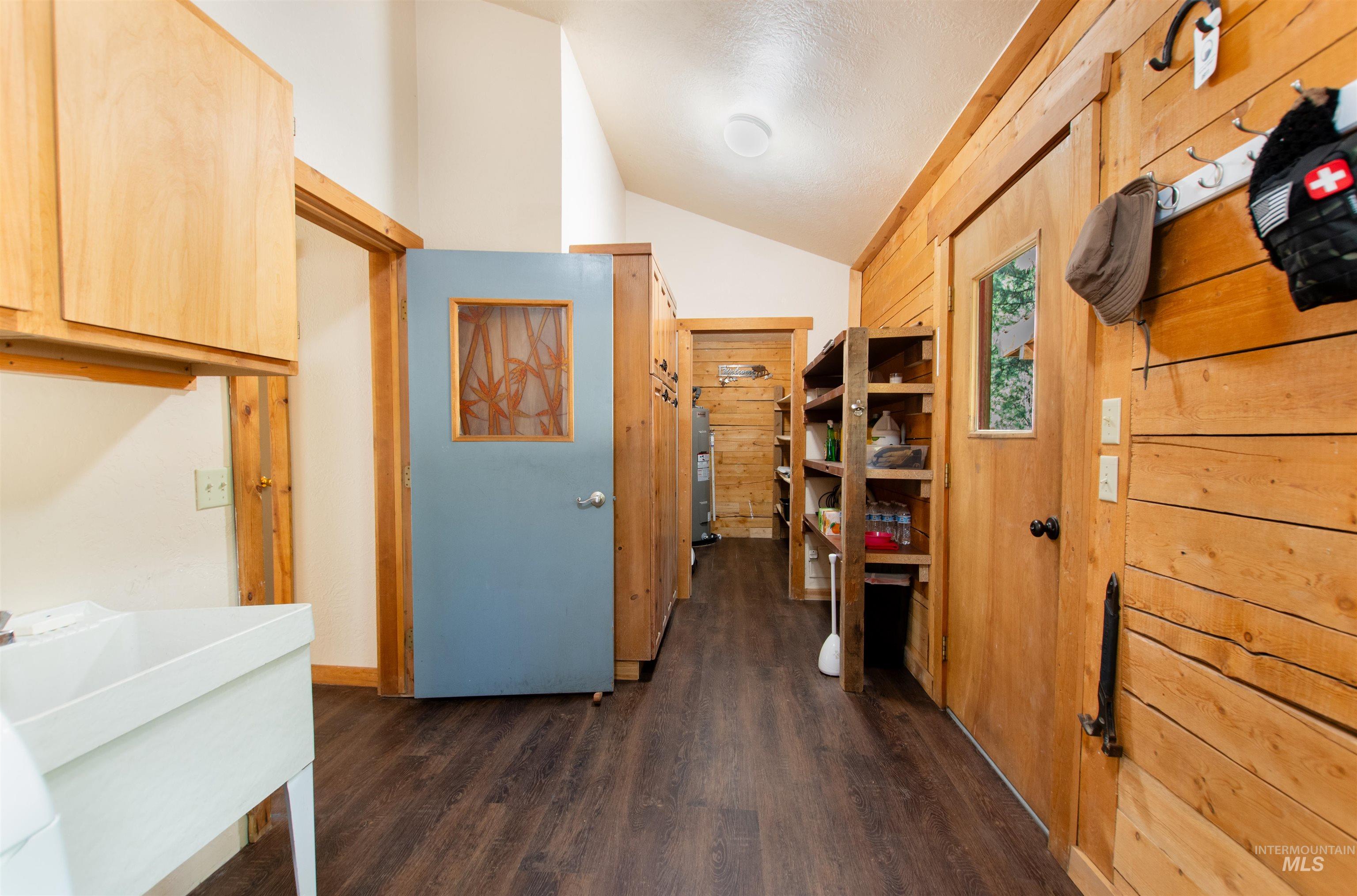 Hallway featuring vaulted ceiling, dark wood-style flooring, wood walls, and a textured ceiling