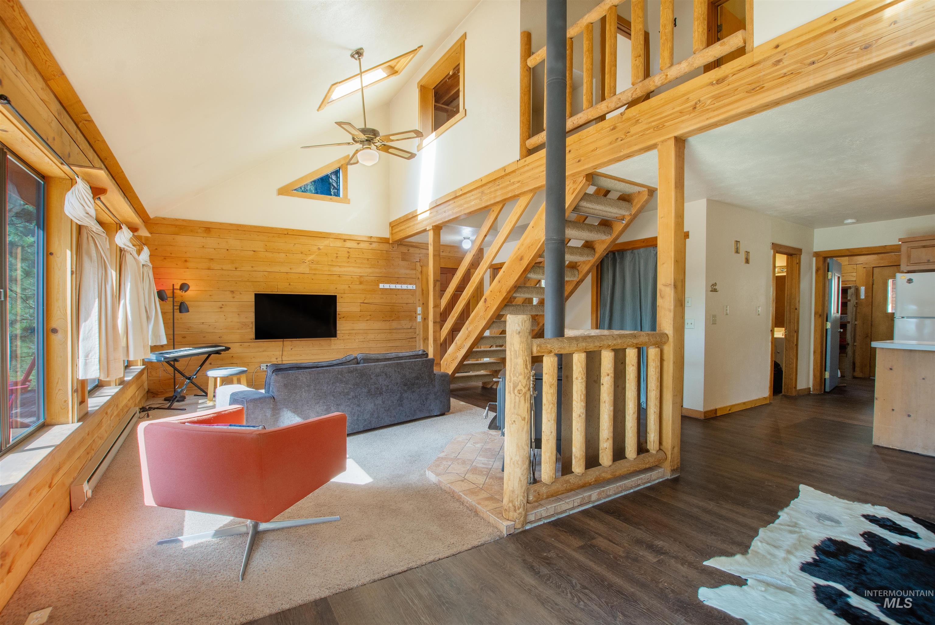 Living room with high vaulted ceiling, wood finished floors, stairway, wooden walls, and ceiling fan