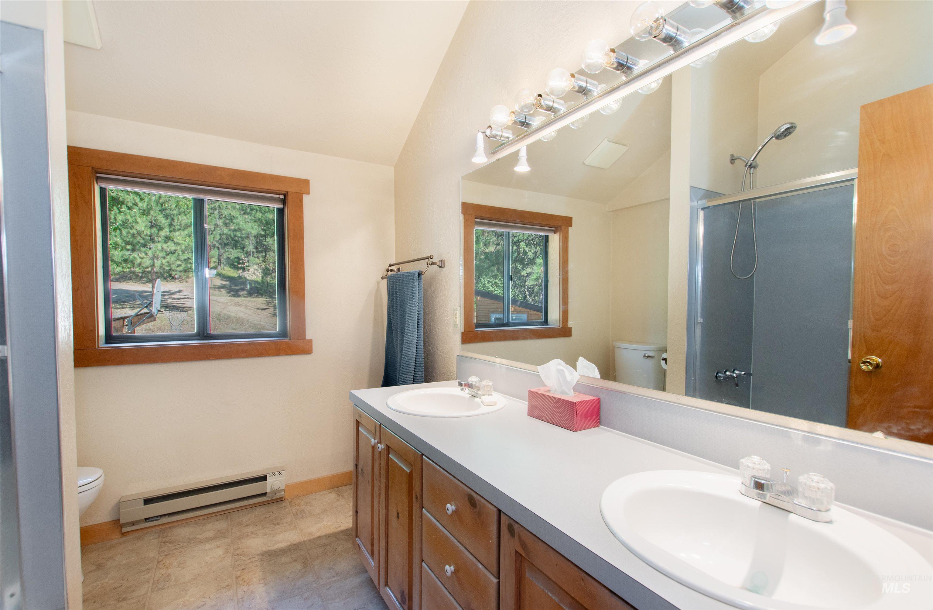 Full bathroom featuring baseboard heating, lofted ceiling, a shower, and double vanity
