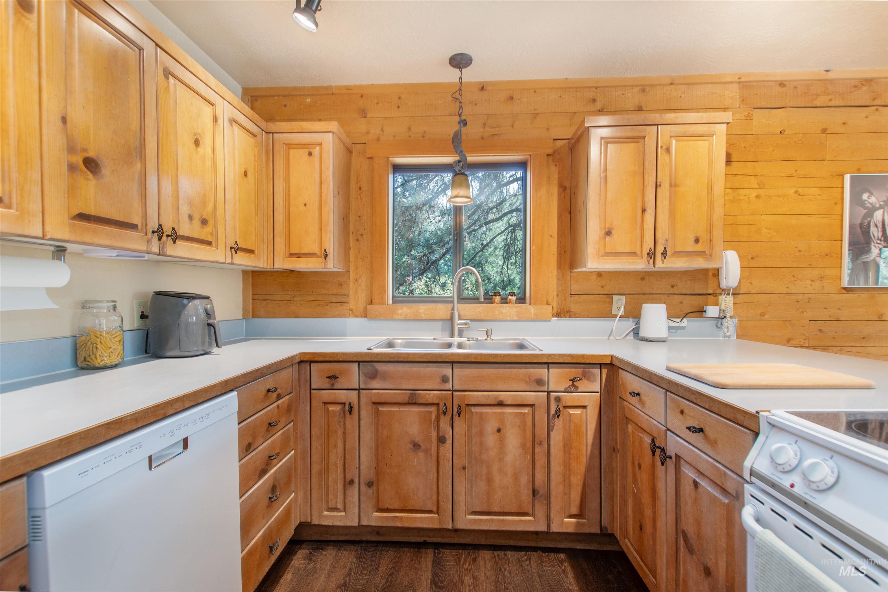 Kitchen featuring white appliances, dark wood-style flooring, pendant lighting, light countertops, and wooden walls