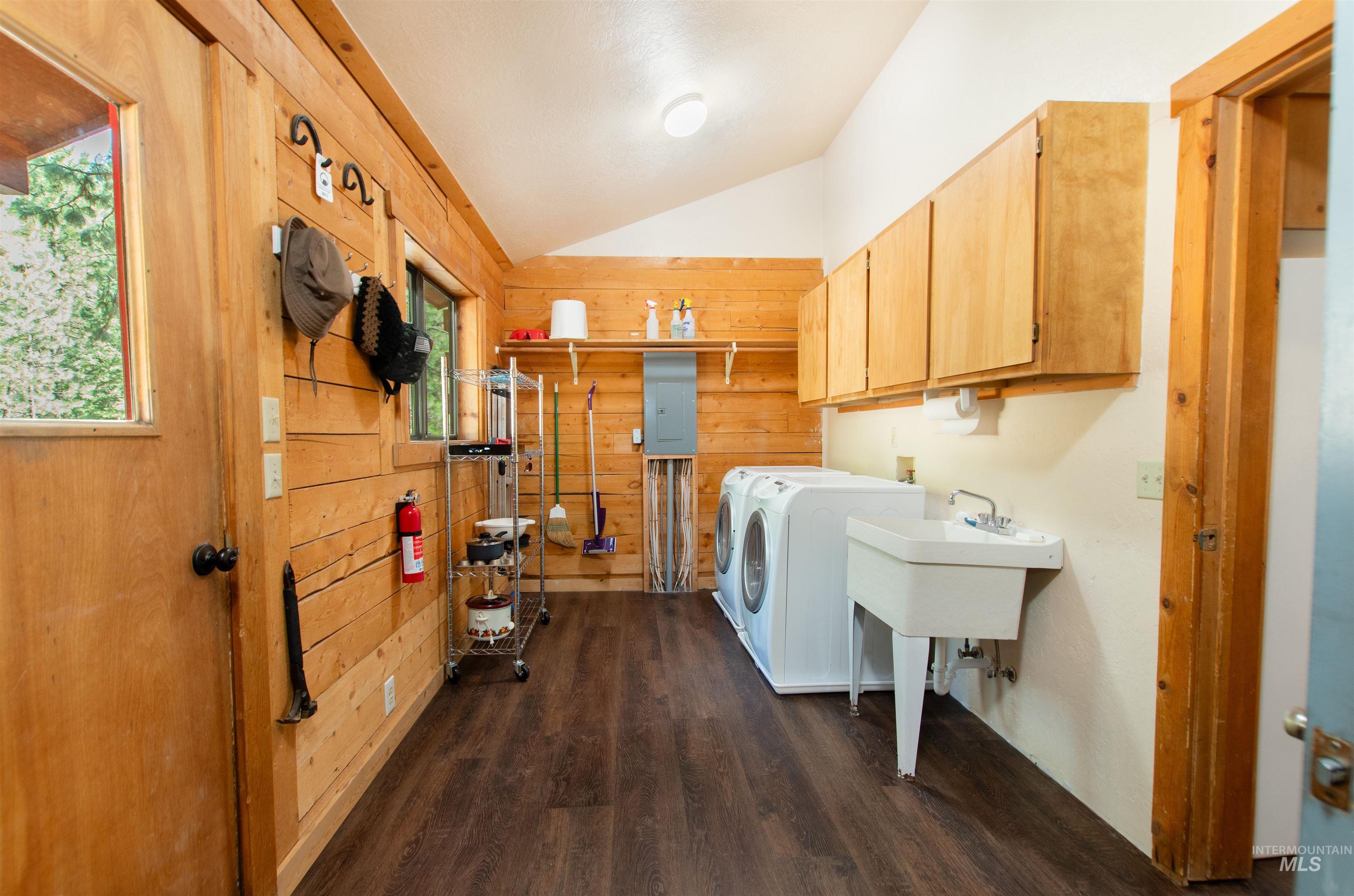 Washroom with cabinet space, washing machine and dryer, dark wood-type flooring, wooden walls, and electric panel
