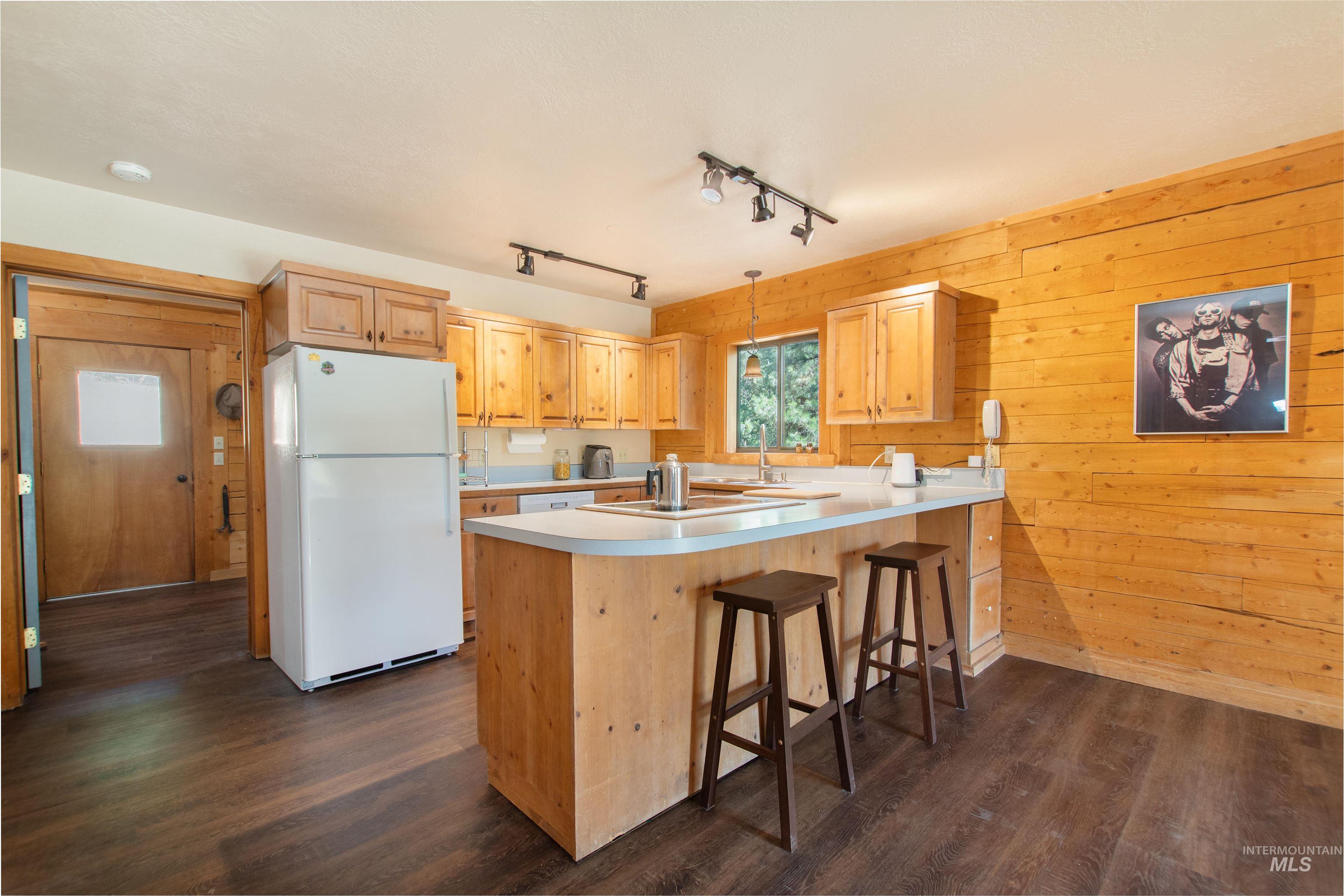 Kitchen with freestanding refrigerator, a peninsula, light countertops, dark wood finished floors, and wooden walls