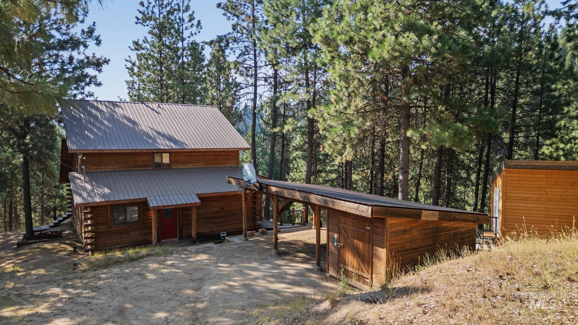 View of front of house featuring a metal roof, dirt driveway, a carport, and an outbuilding