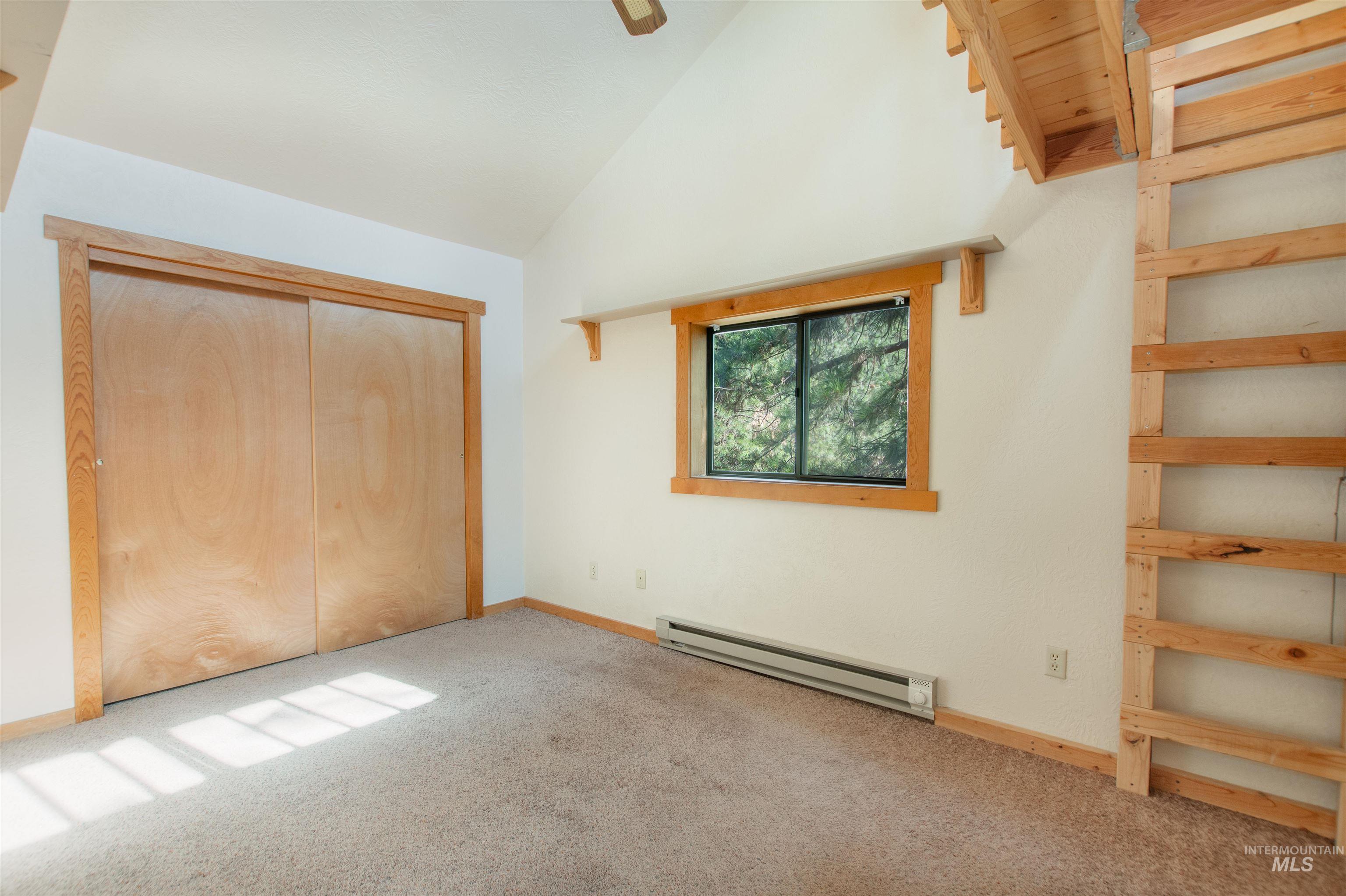 Unfurnished bedroom featuring carpet, baseboard heating, a closet, high vaulted ceiling, and ceiling fan