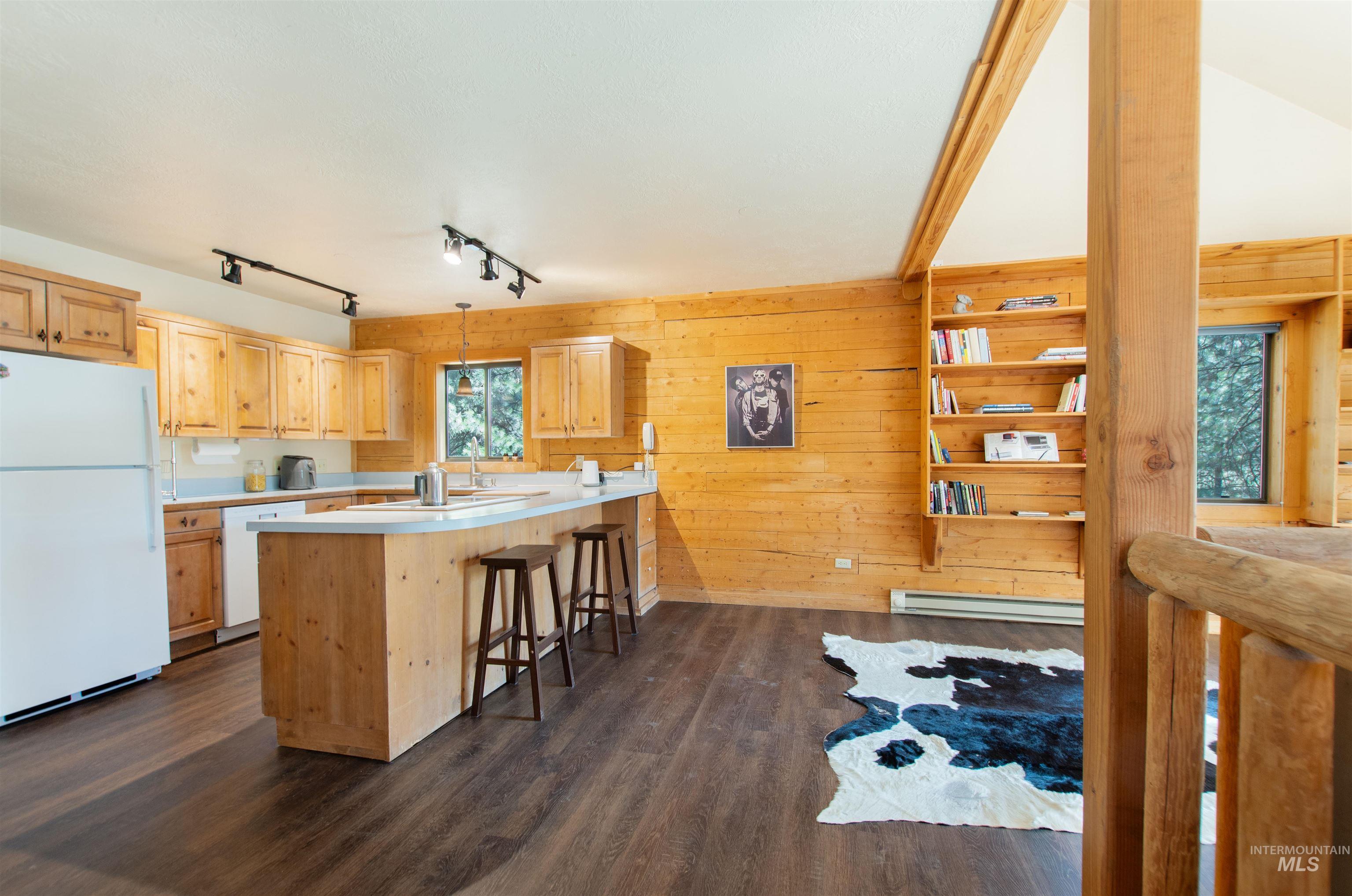 Kitchen with white appliances, light countertops, a peninsula, light brown cabinets, and wood walls