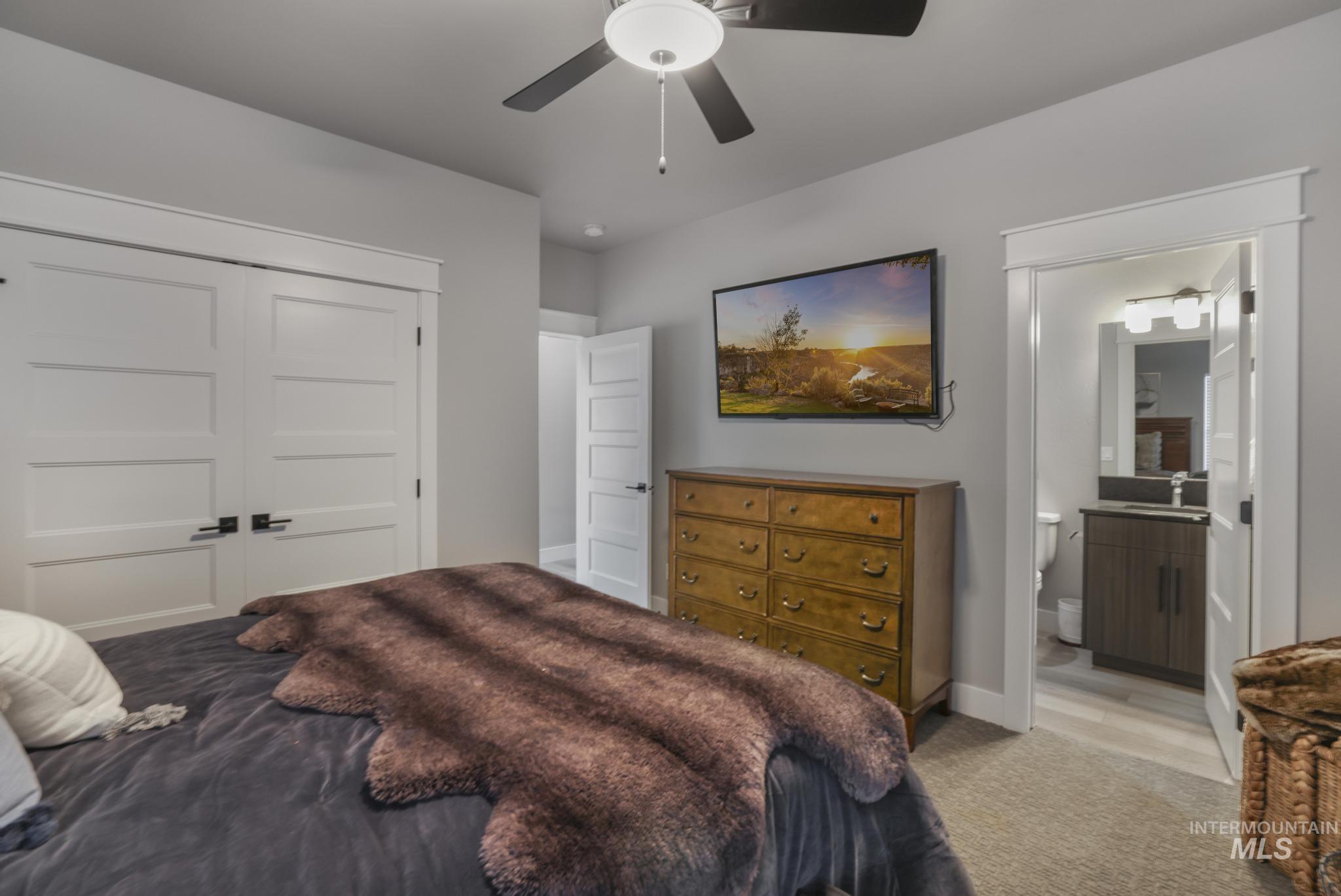 Carpeted bedroom with a closet, ceiling fan, and ensuite bath