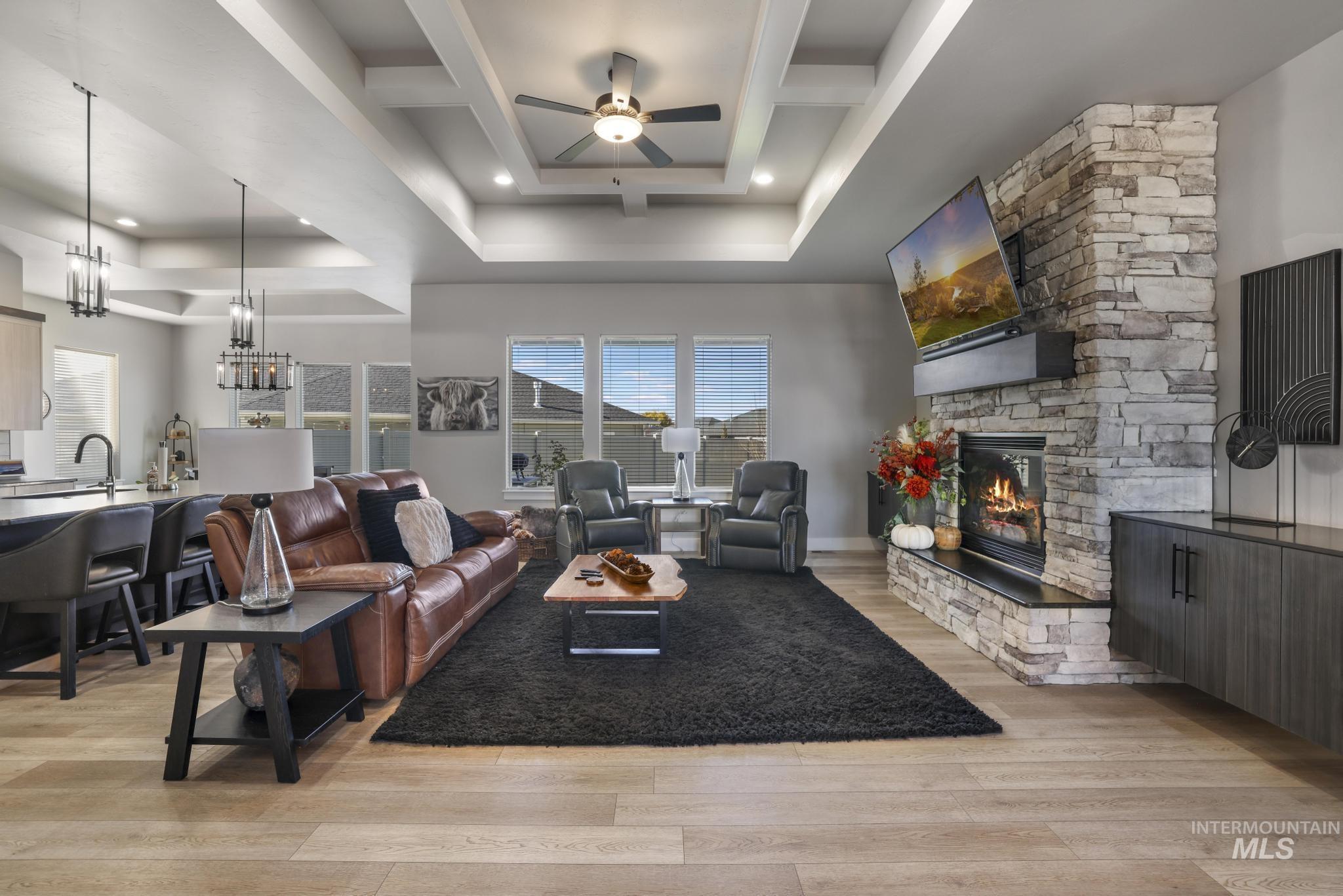 Living area with light wood finished floors, ceiling fan, a stone fireplace, a chandelier, and recessed lighting