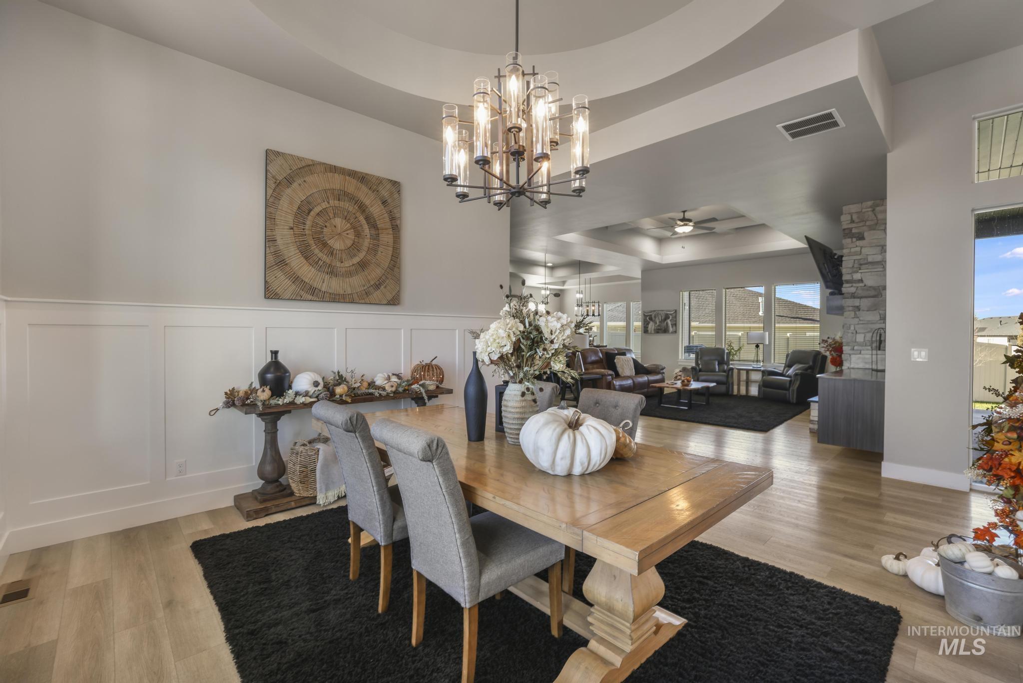 Dining space with a raised ceiling, a ceiling fan, light wood-type flooring, a chandelier, and a decorative wall