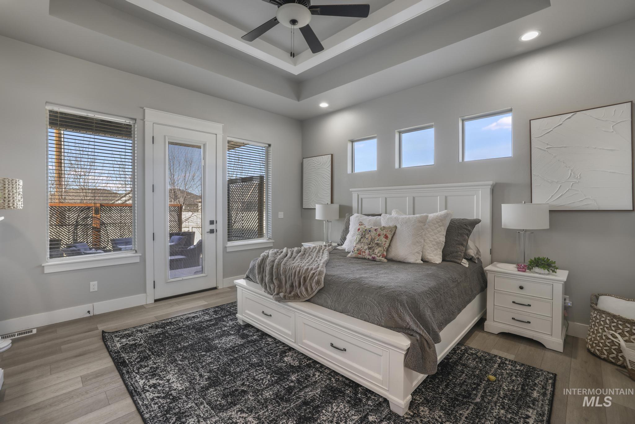 Bedroom featuring access to outside, light wood finished floors, a ceiling fan, a tray ceiling, and recessed lighting
