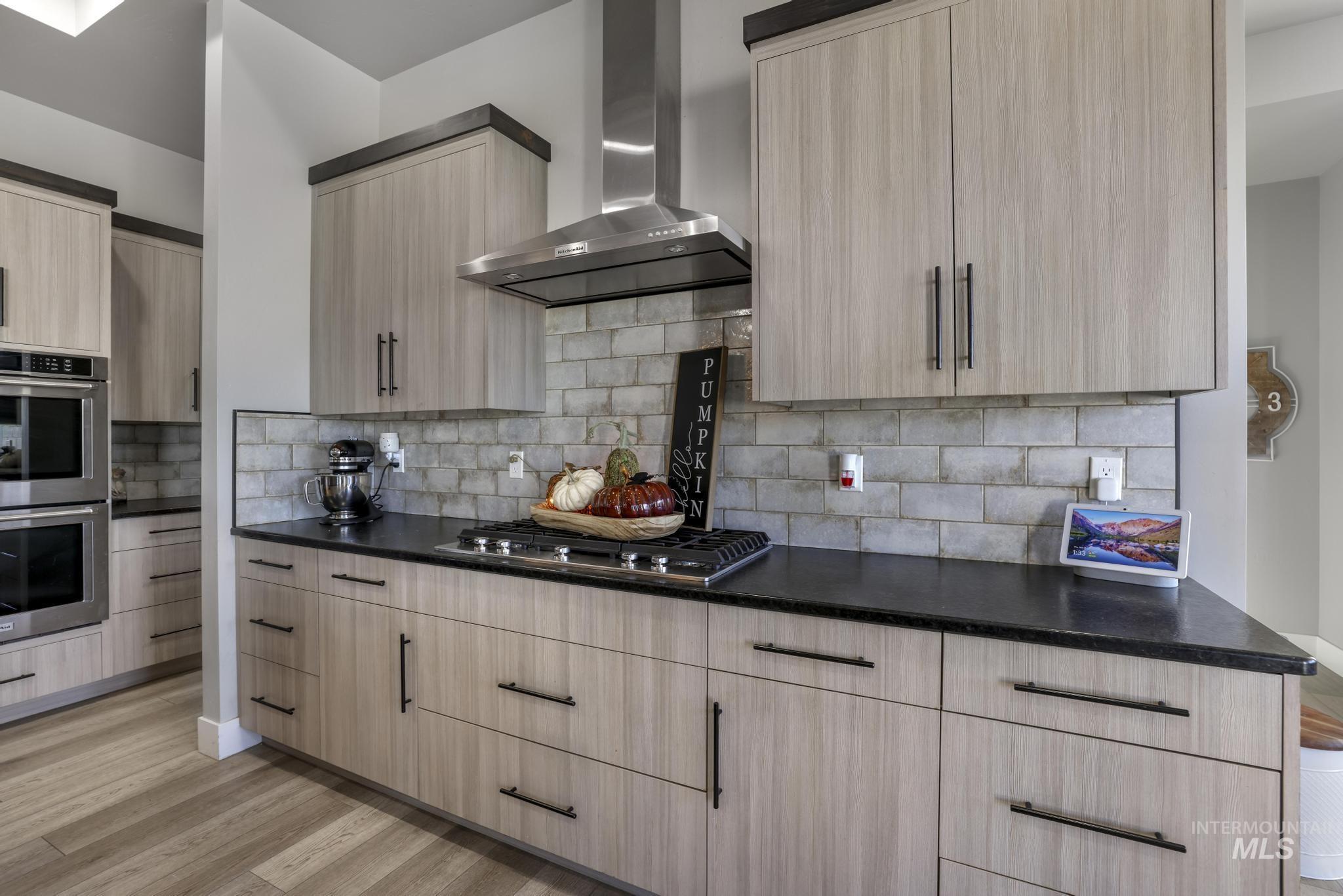 Kitchen featuring light brown cabinetry, wall chimney range hood, appliances with stainless steel finishes, light wood-style flooring, and modern cabinets