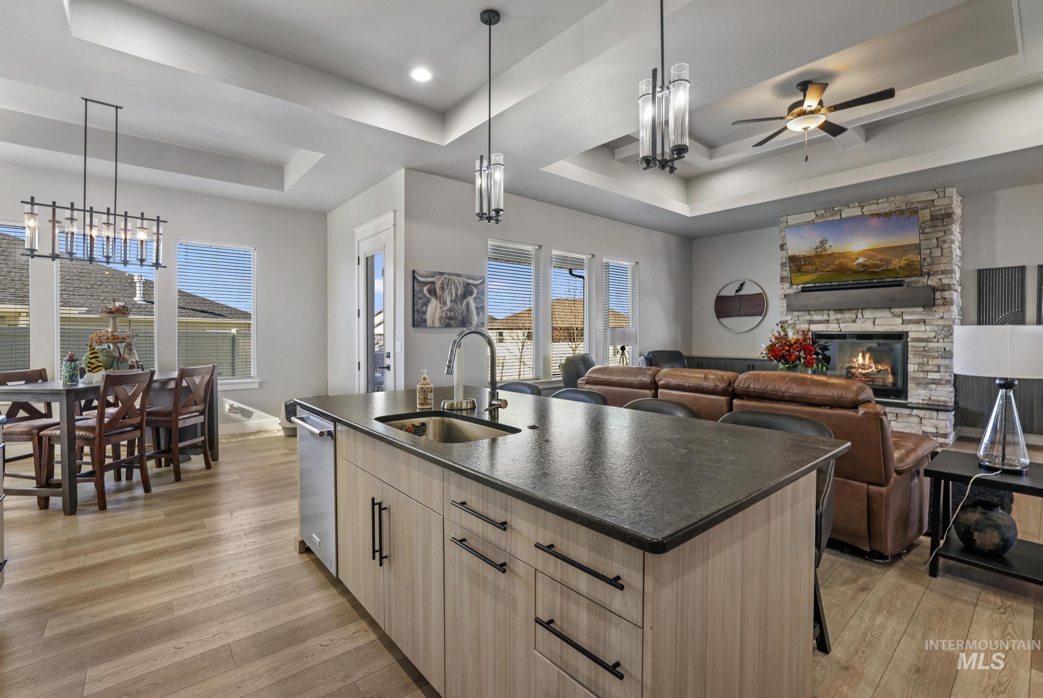 Kitchen featuring light wood-style floors, a tray ceiling, a center island with sink, and a fireplace
