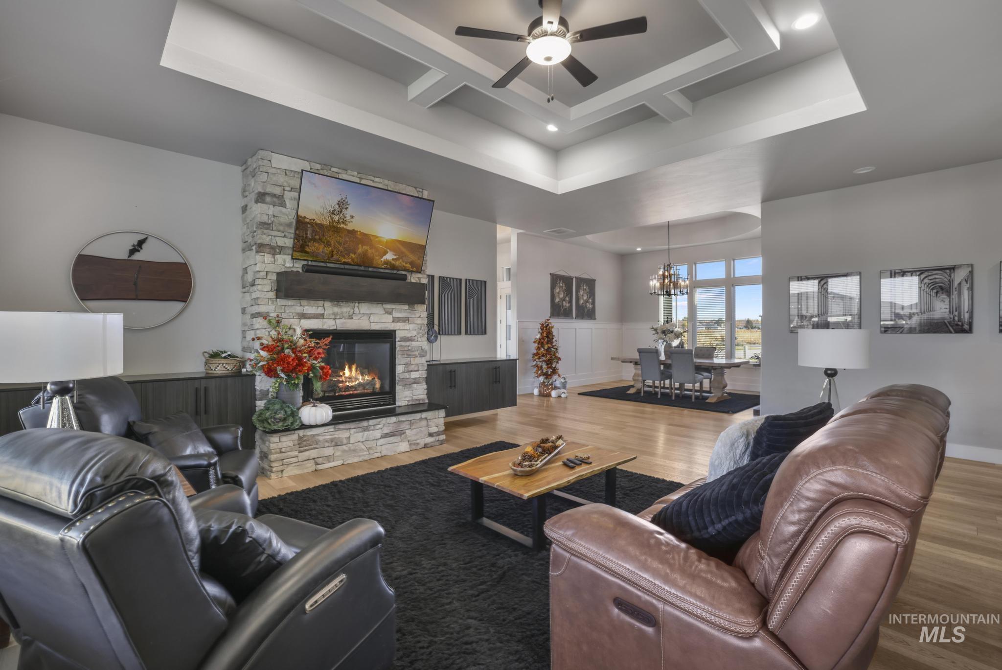 Living area featuring a stone fireplace, coffered ceiling, wainscoting, wood finished floors, and a ceiling fan