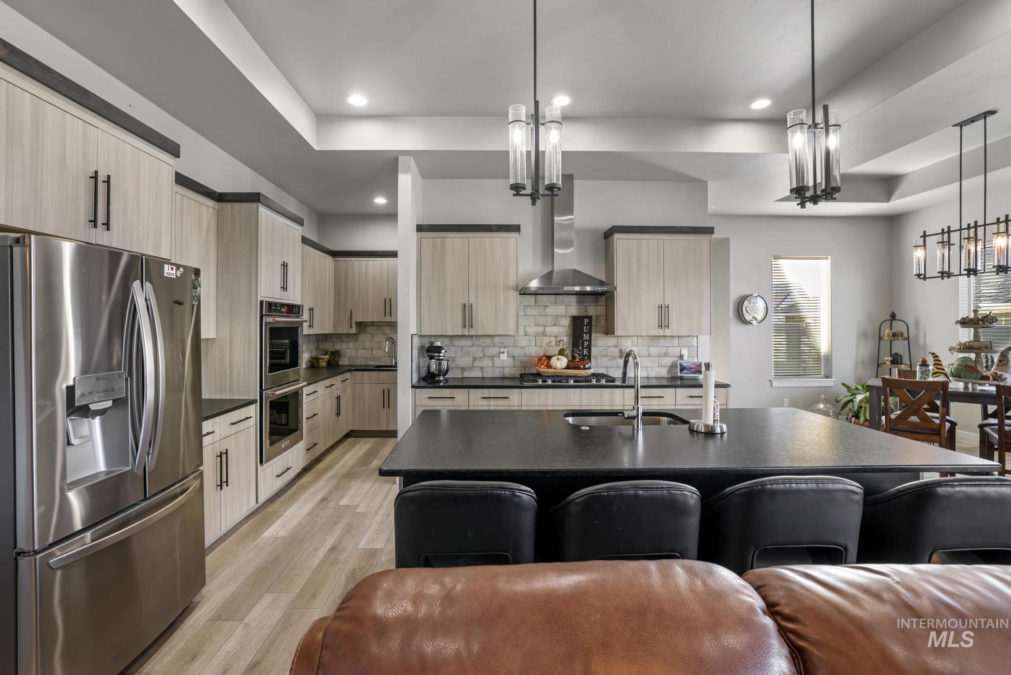 Kitchen featuring stainless steel appliances, light brown cabinets, a center island with sink, pendant lighting, and light wood-style flooring