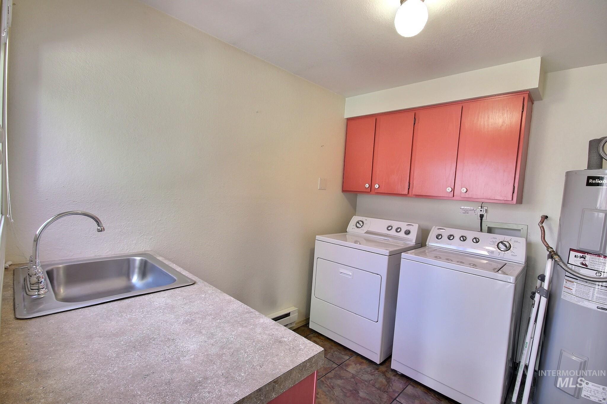 Washroom with electric water heater, cabinet space, separate washer and dryer, a baseboard radiator, and dark tile patterned floors